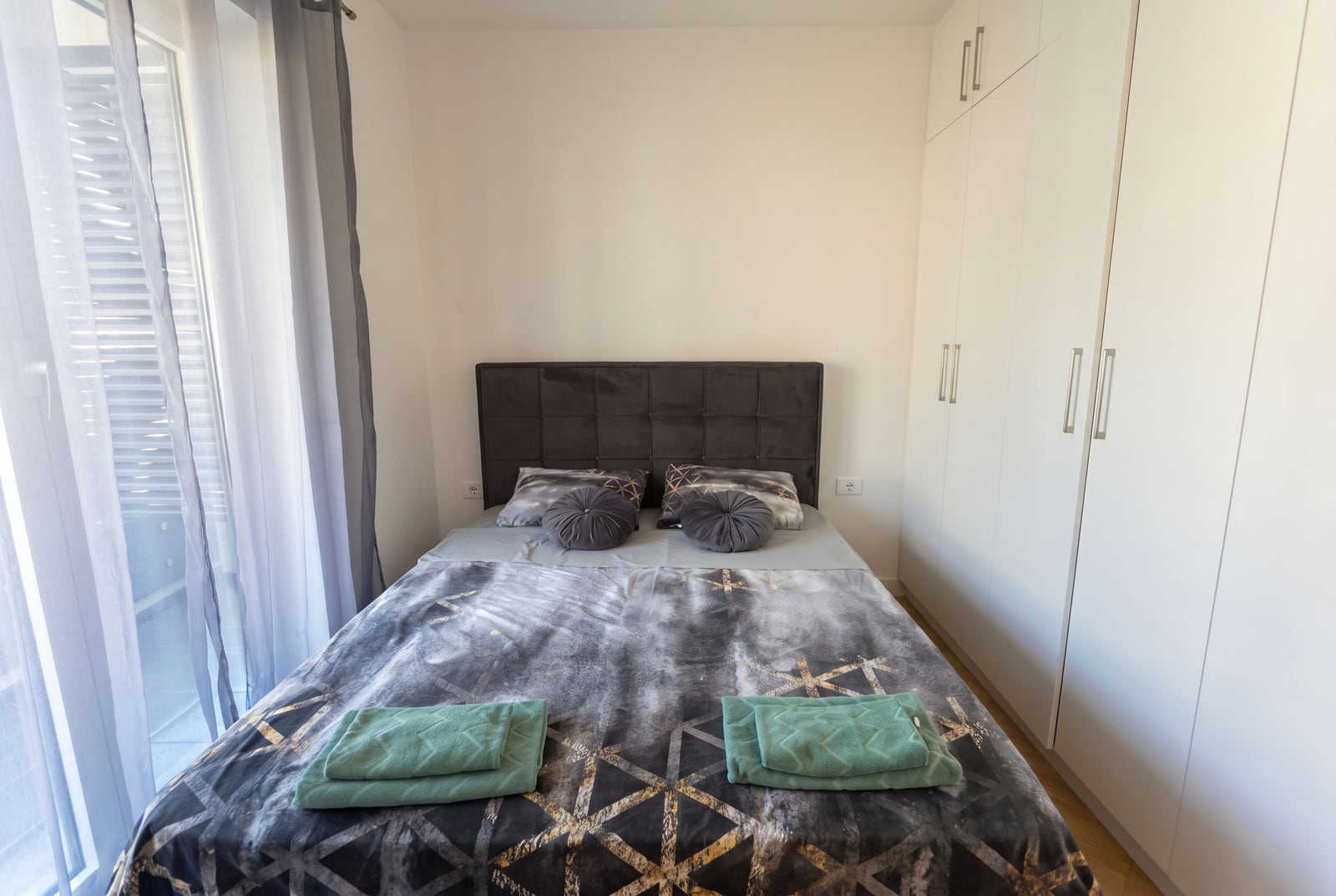 Bedroom in an apartment in Bečići, Montenegro: double bed with a padded headboard and a built-in white wardrobe.