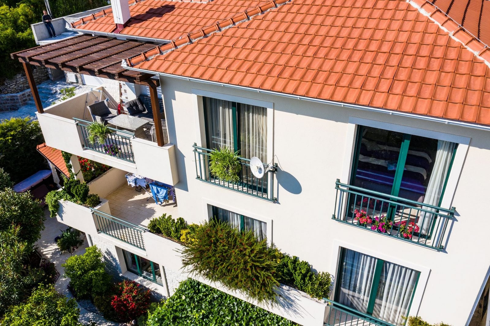 View of the villa facade in Tivat, Montenegro: terraces with furniture, tiled roof, and landscaping from above.