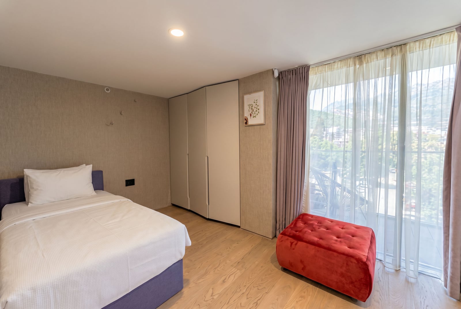 Modern bedroom in a Budva apartment, Montenegro: double bed, built-in wardrobe, and mountain view from the balcony.