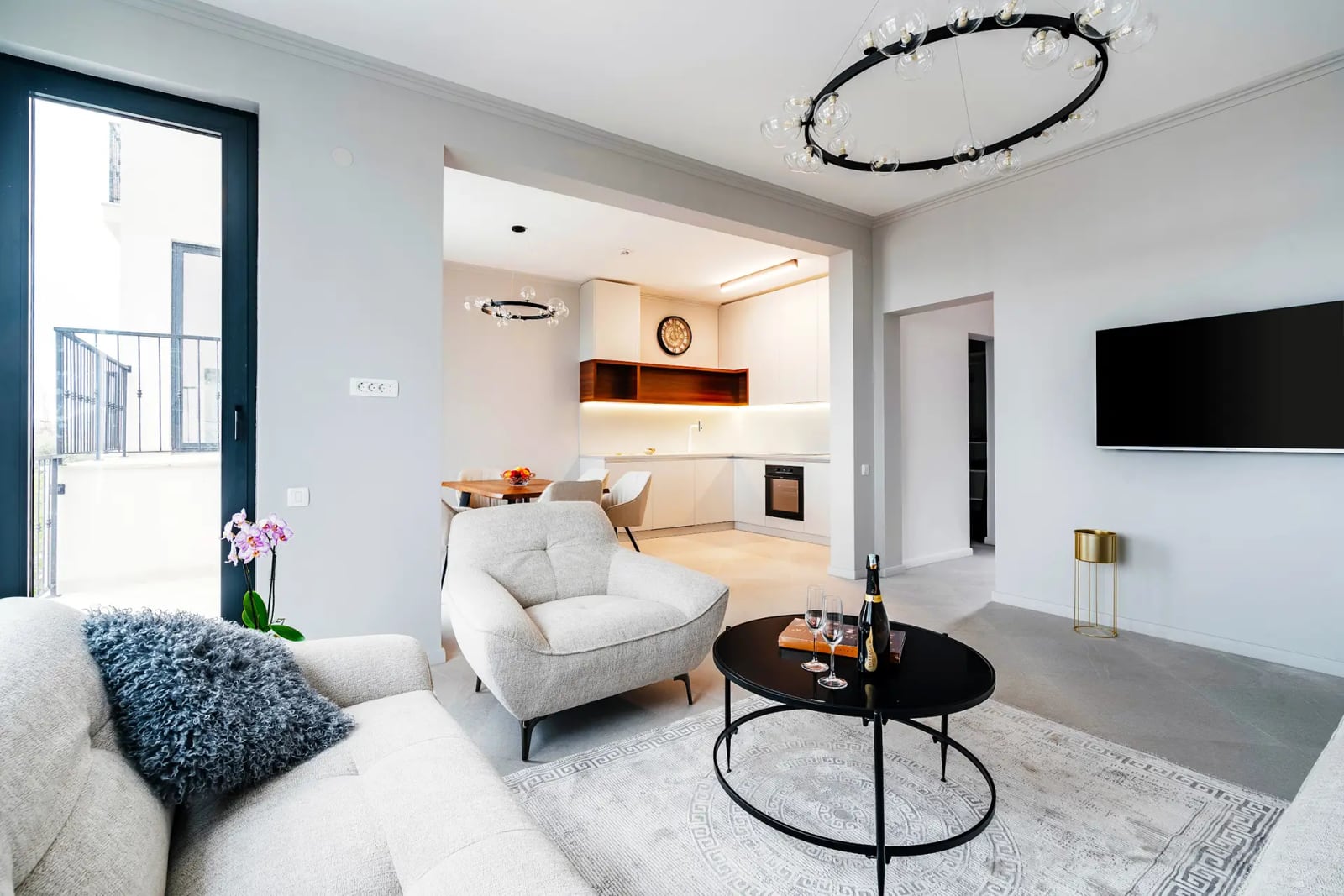 Modern living room with a kitchen in a villa in Reževići, Montenegro: light-colored furniture, designer lighting, and a balcony.