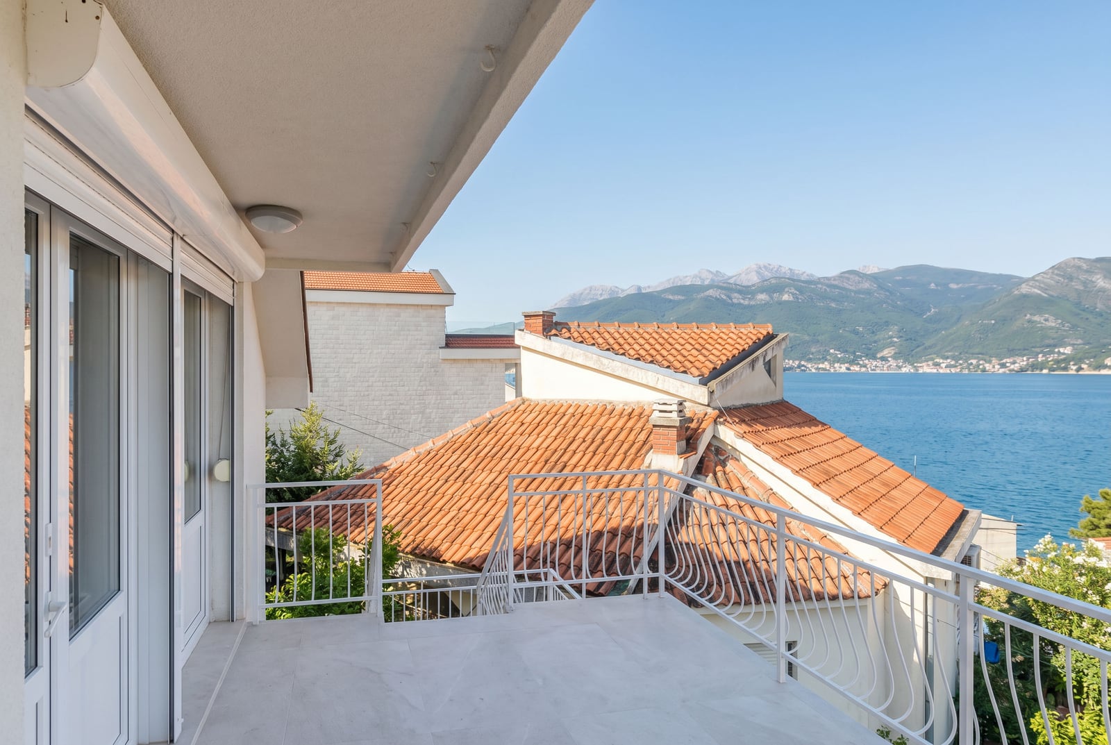 Spacious balcony with a sea and mountain view in a house, Krašići, Montenegro: light-colored finishes and wrought-iron railing.