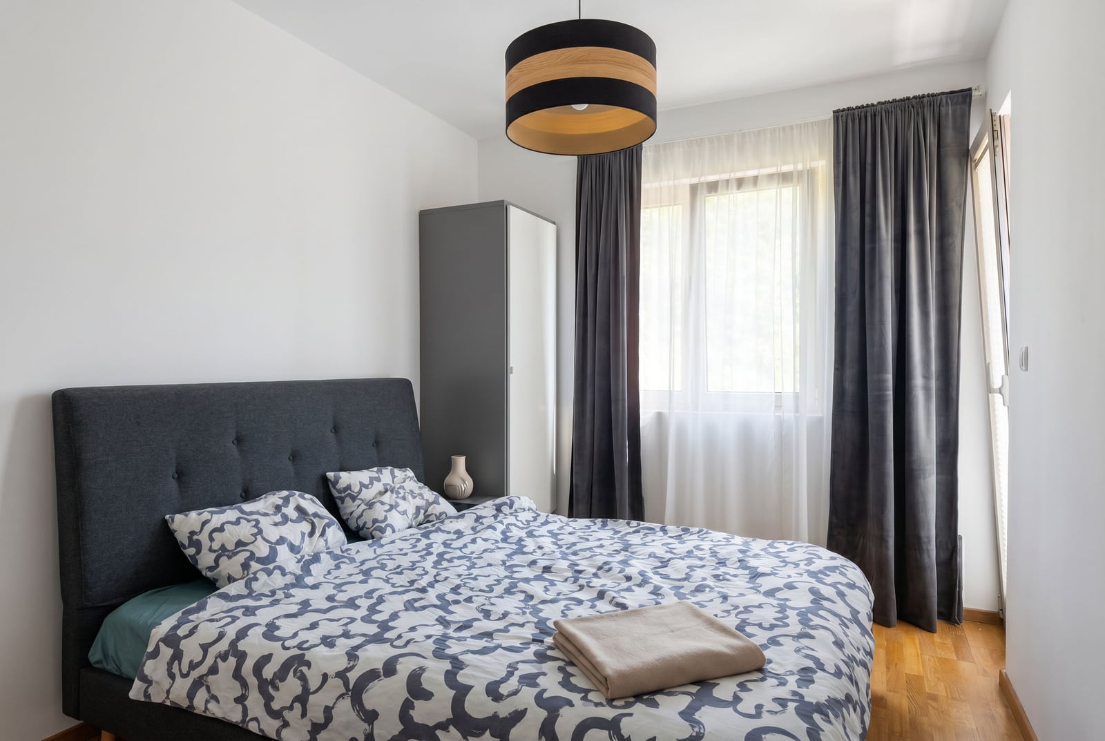 Modern bedroom with a double bed and wardrobe in an apartment in Becici, Montenegro, featuring parquet flooring and curtains.