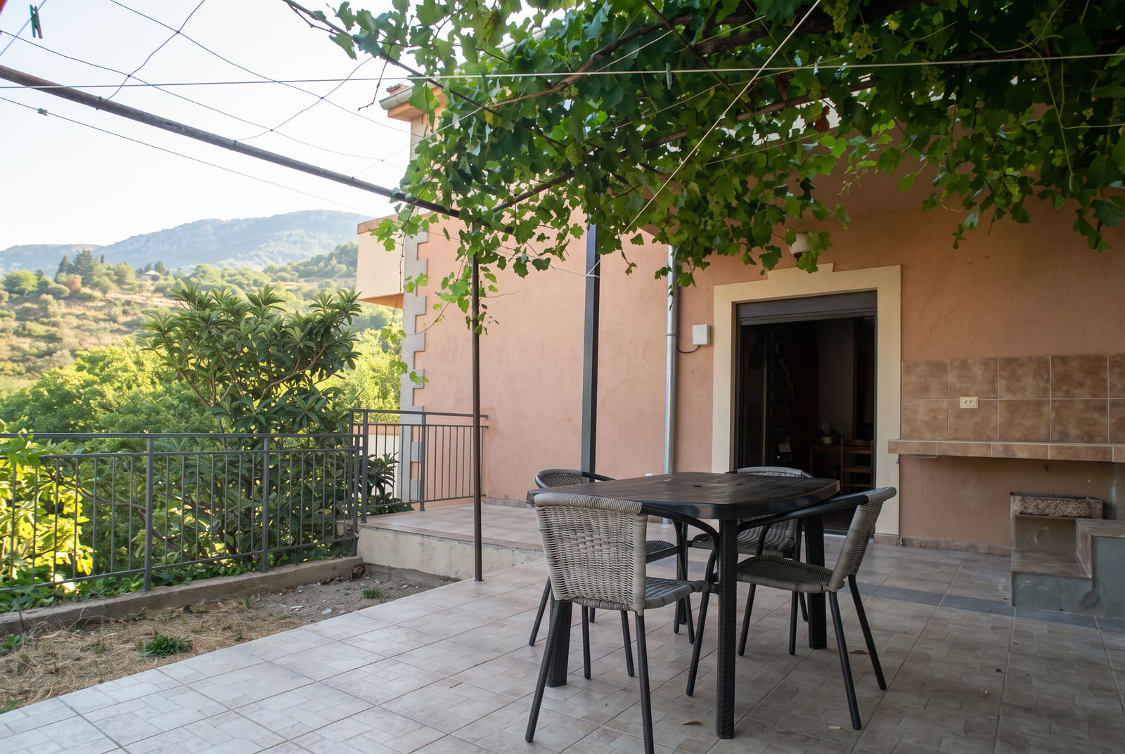 Cozy house terrace in Tivat, Montenegro, with garden furniture and a vine pergola overlooking the mountains.