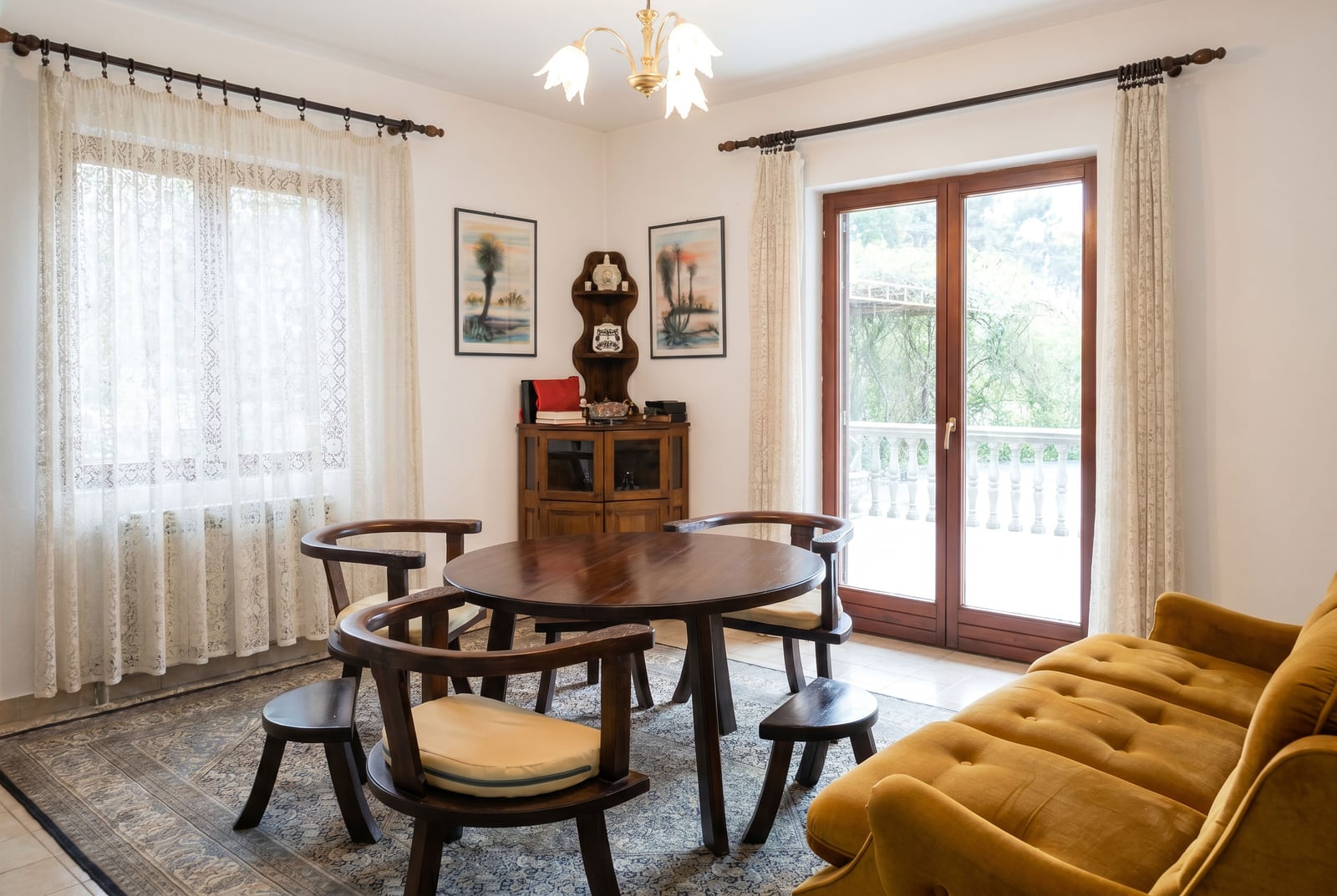 Living room with wooden furniture and a yellow sofa in a house in Lastva, Montenegro, with access to a terrace and garden view.