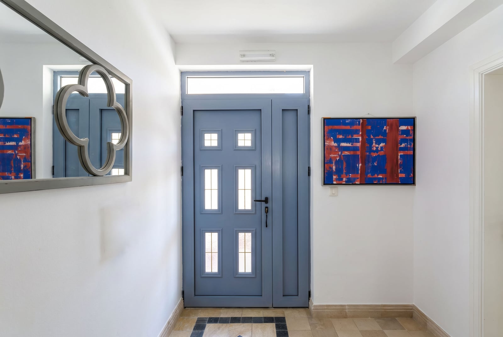 Bright hallway in a penthouse in Risan, Montenegro: blue entrance door, mirror, and painting on white walls.