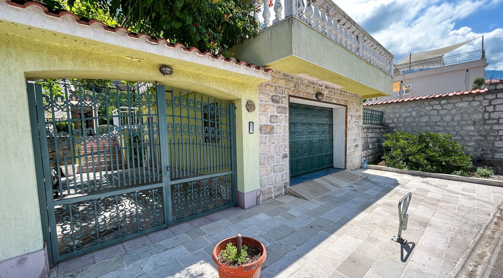 Villa facade in Dobrota, Montenegro: stone cladding, garage doors, and wrought-iron gates with a terrace on the second floor.