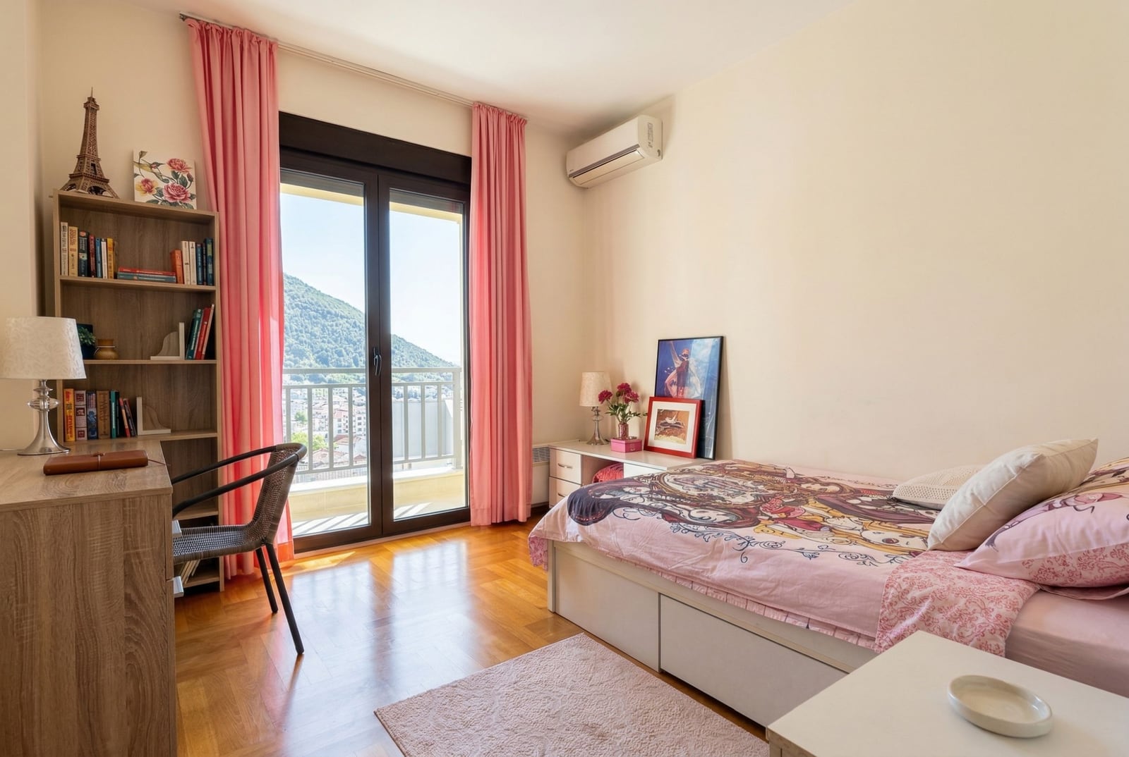 Bedroom in an apartment in Budva, Montenegro: bed, desk, shelving unit, parquet flooring, and access to a balcony with mountain views.