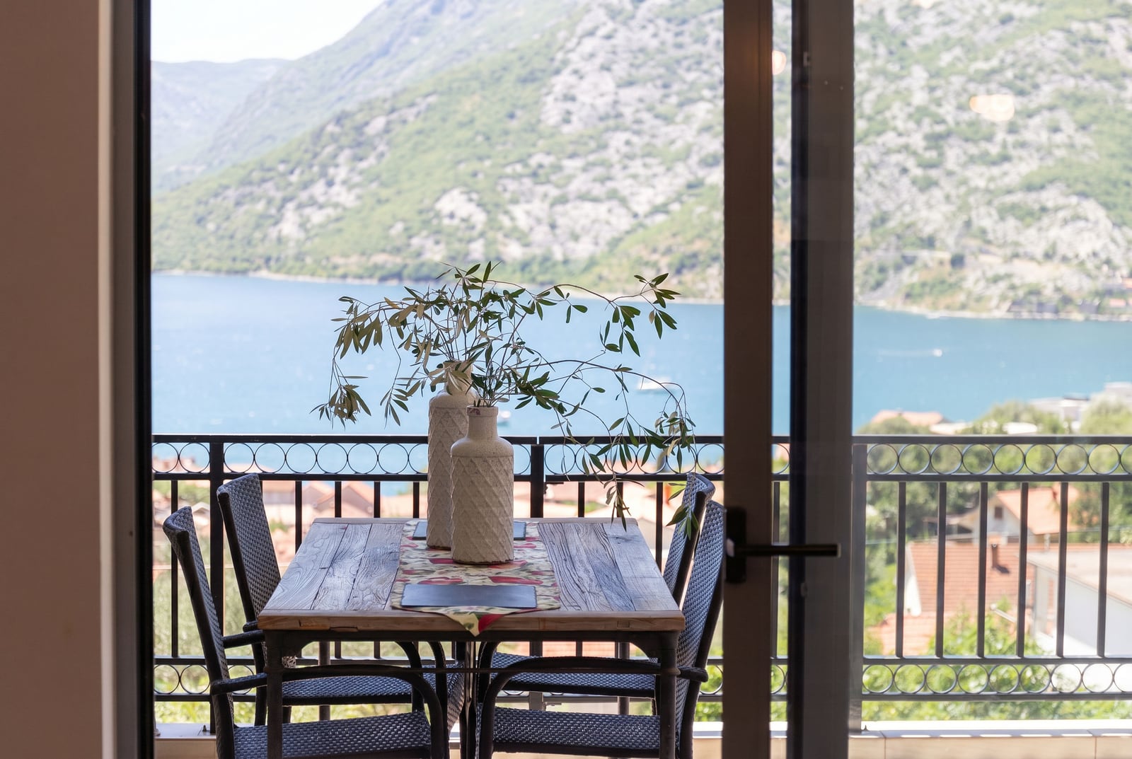 View from the balcony of an apartment in Risan, Montenegro: a wooden table, wicker chairs, and a panoramic view of the Bay of Kotor.