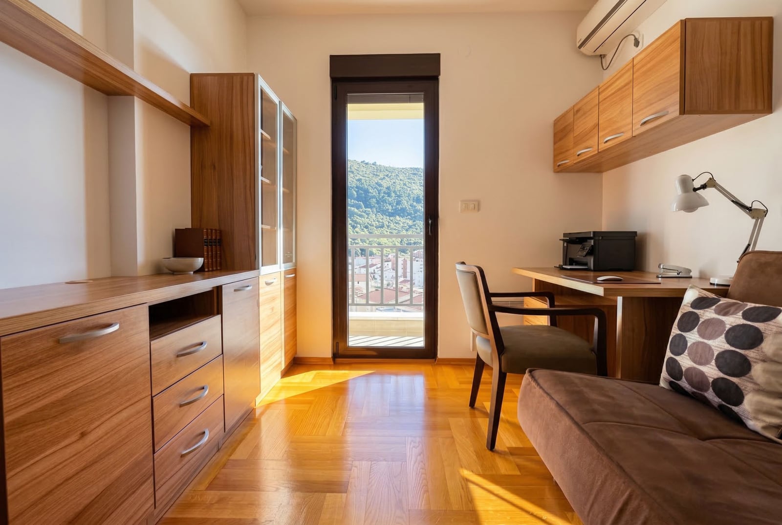Home office in an apartment in Budva, Montenegro: wooden furniture, parquet flooring, and a balcony with mountain and city views.