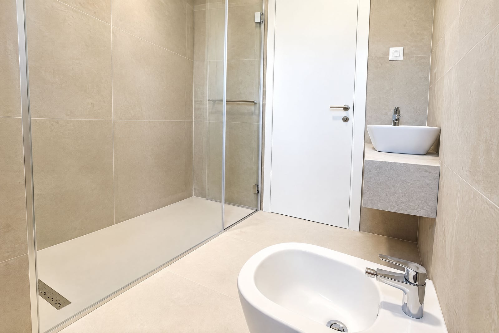 Modern bathroom featuring a glass shower enclosure, floor bidet, and vessel sink on beige tiled walls.