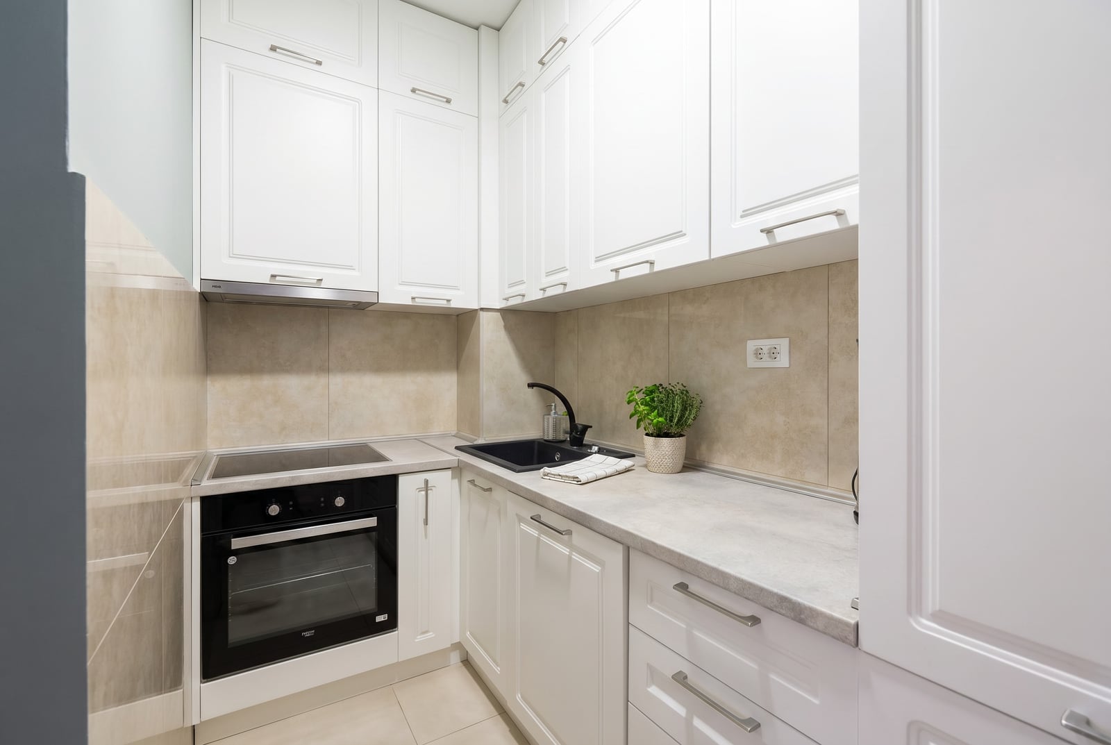 Modern white kitchen in a Budva, Montenegro apartment: built-in appliances, dark sink, and light wall finishes.