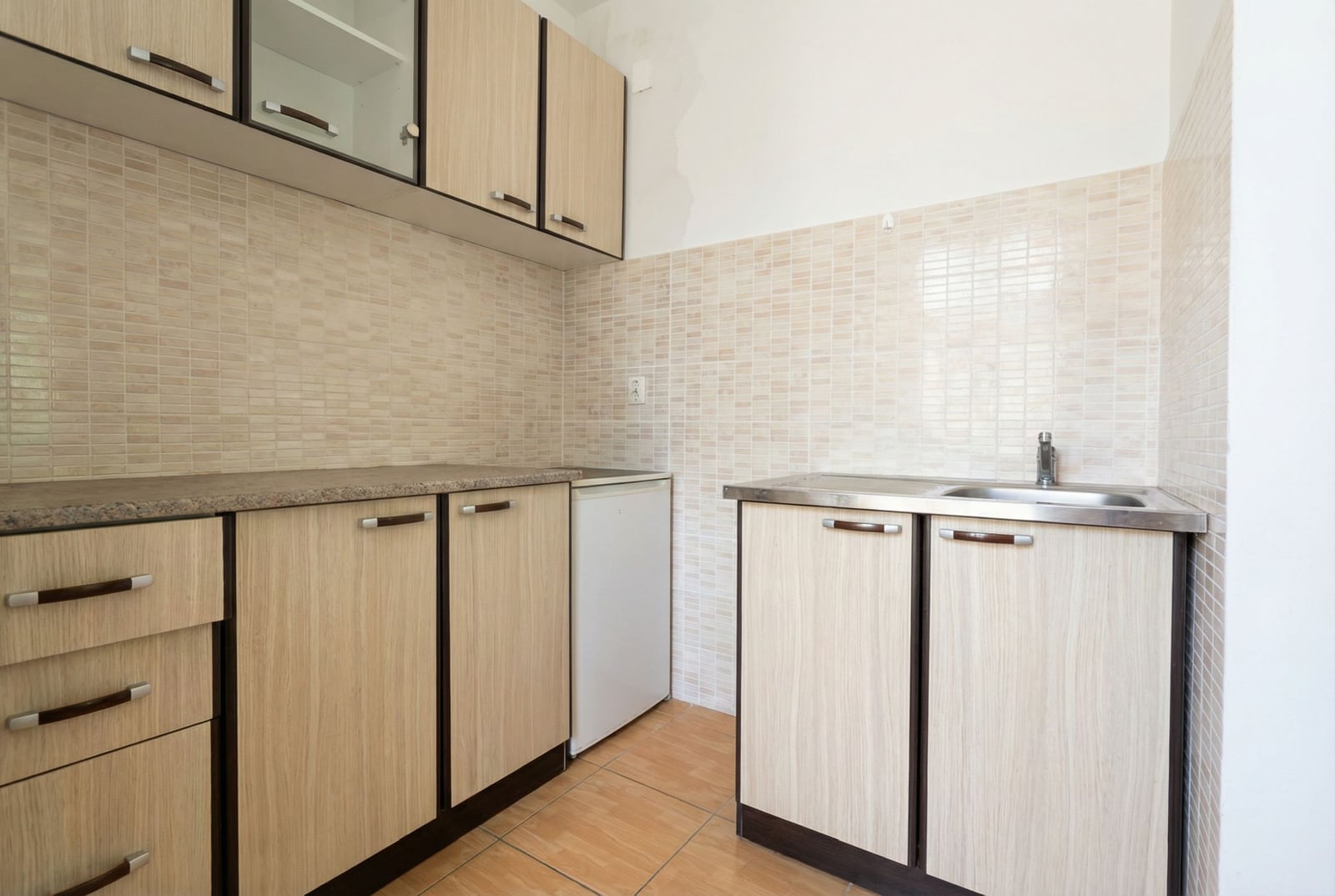 Studio kitchen in Budva, Montenegro: light wood-look cabinets, tiled backsplash, and built-in sink.