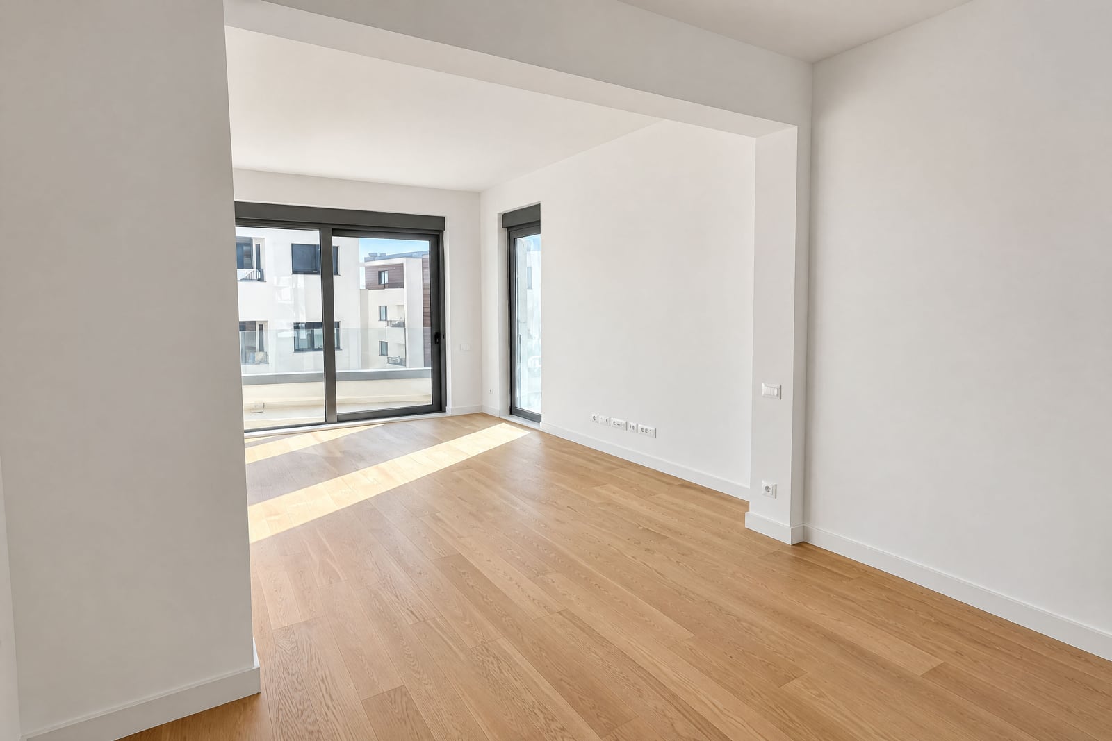 Empty room with light wood flooring, white walls, and a large sliding glass door leading to a balcony.