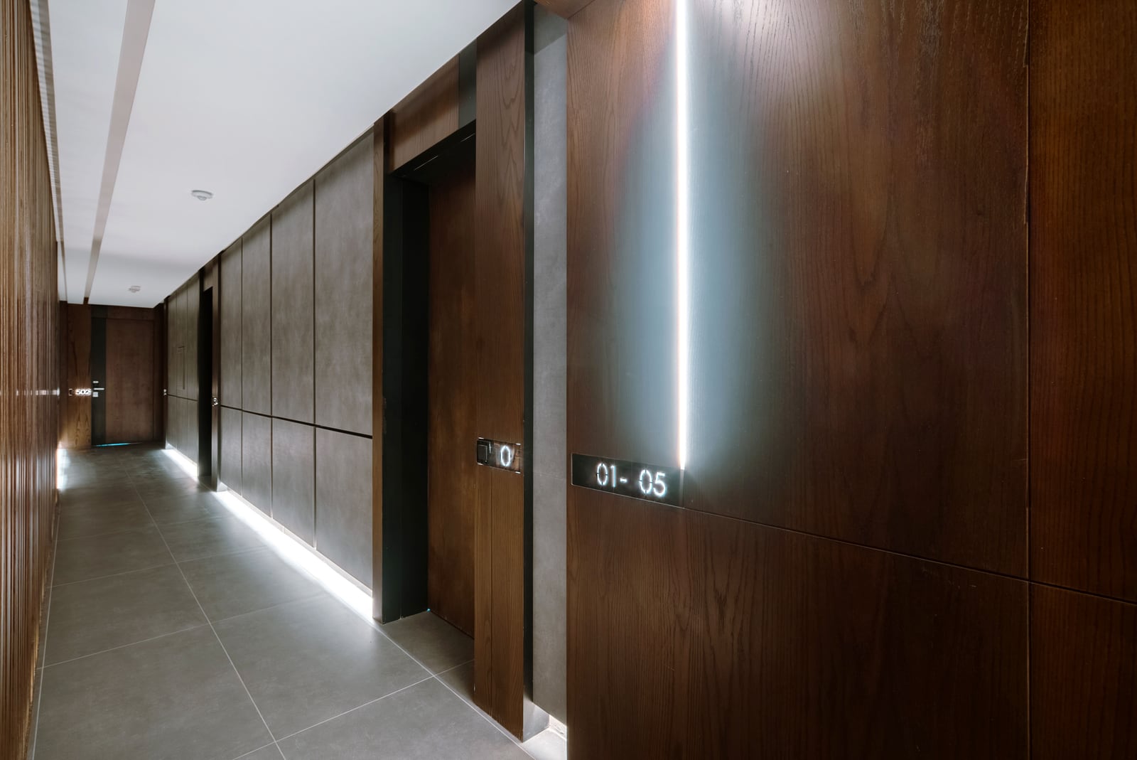 Modern corridor of a residential complex in Bečići, Montenegro: wood finishing, hidden lighting, and stylish door numbers.
