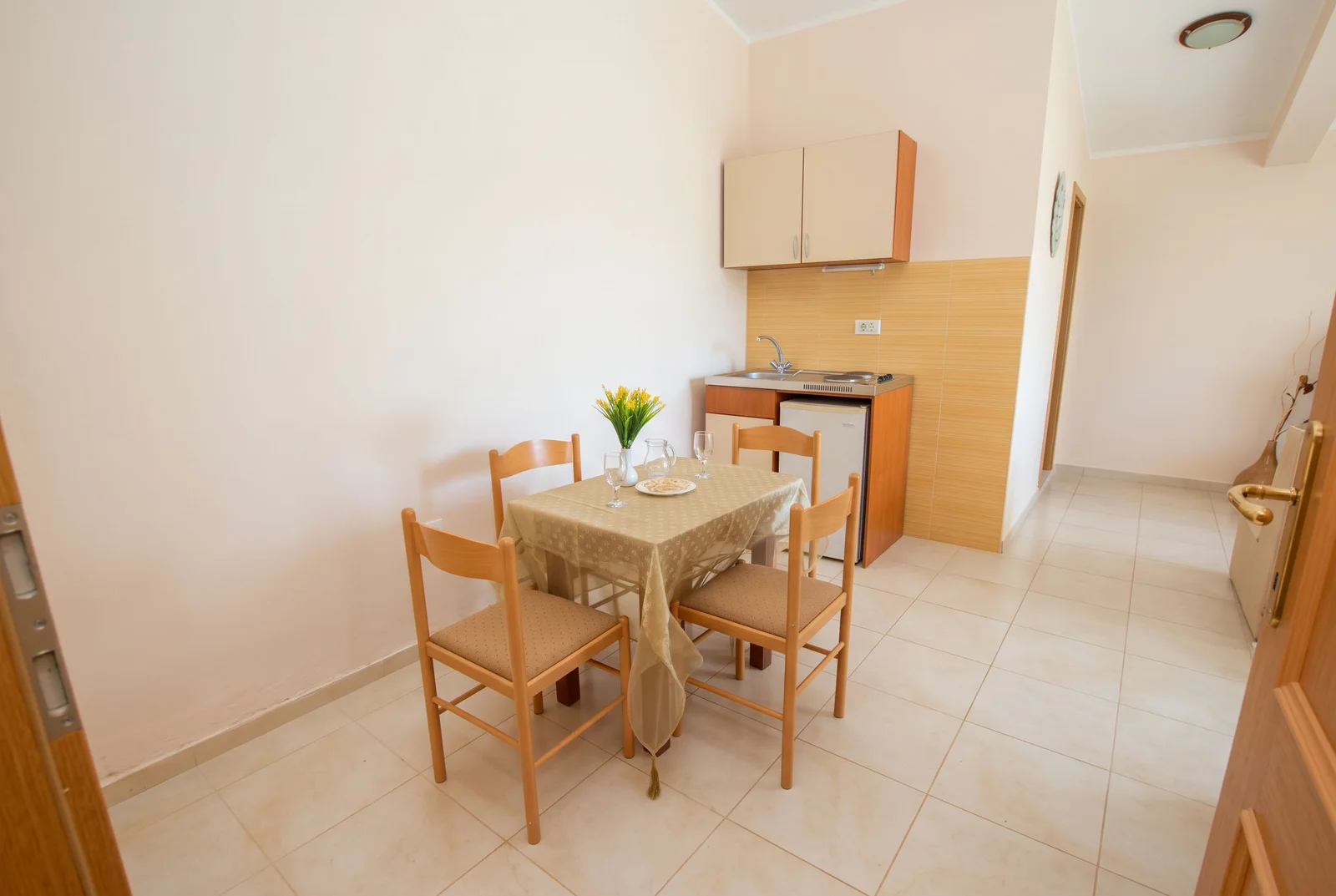 Small kitchen area with a dining table for four, wall cabinets, sink, and mini fridge.