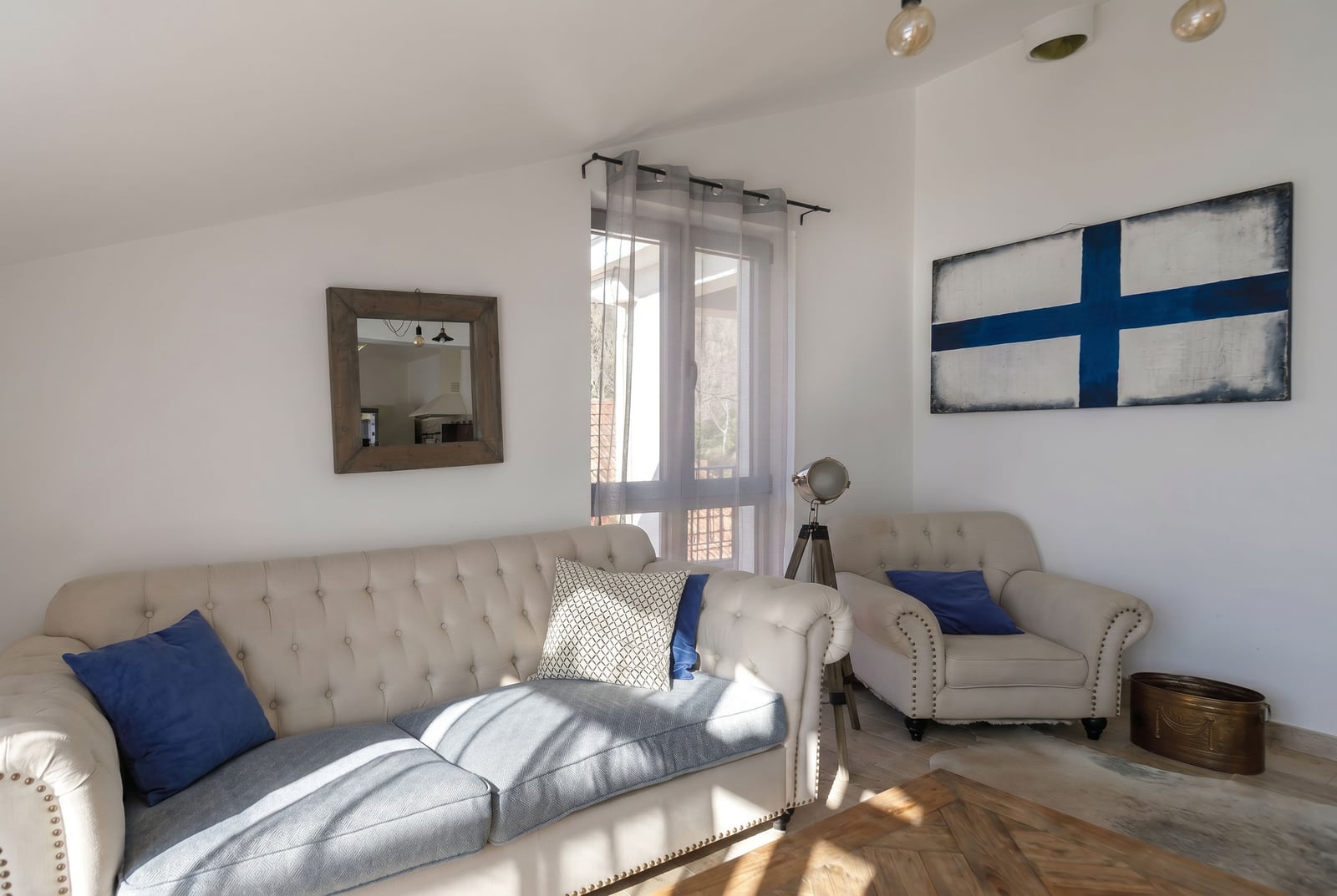 Bright living room in a penthouse in Risan, Montenegro: beige Chesterfield sofa, armchair, mirror, and painting on the wall.