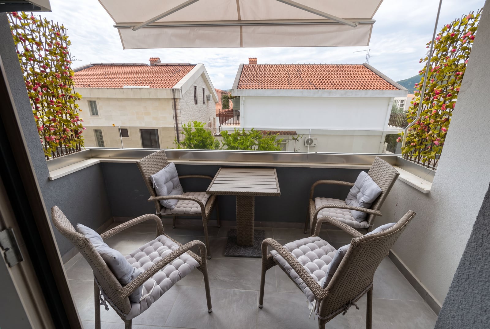 Balcony with wicker furniture, table, umbrella, and view of neighboring rooftops.