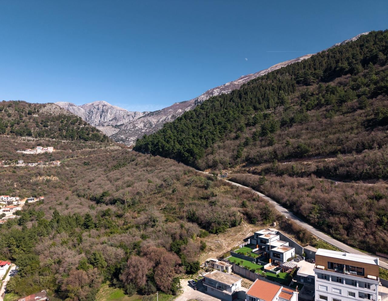 Aerial view of a land plot in Kotor, Montenegro: modern villas at the foot of picturesque mountain slopes.