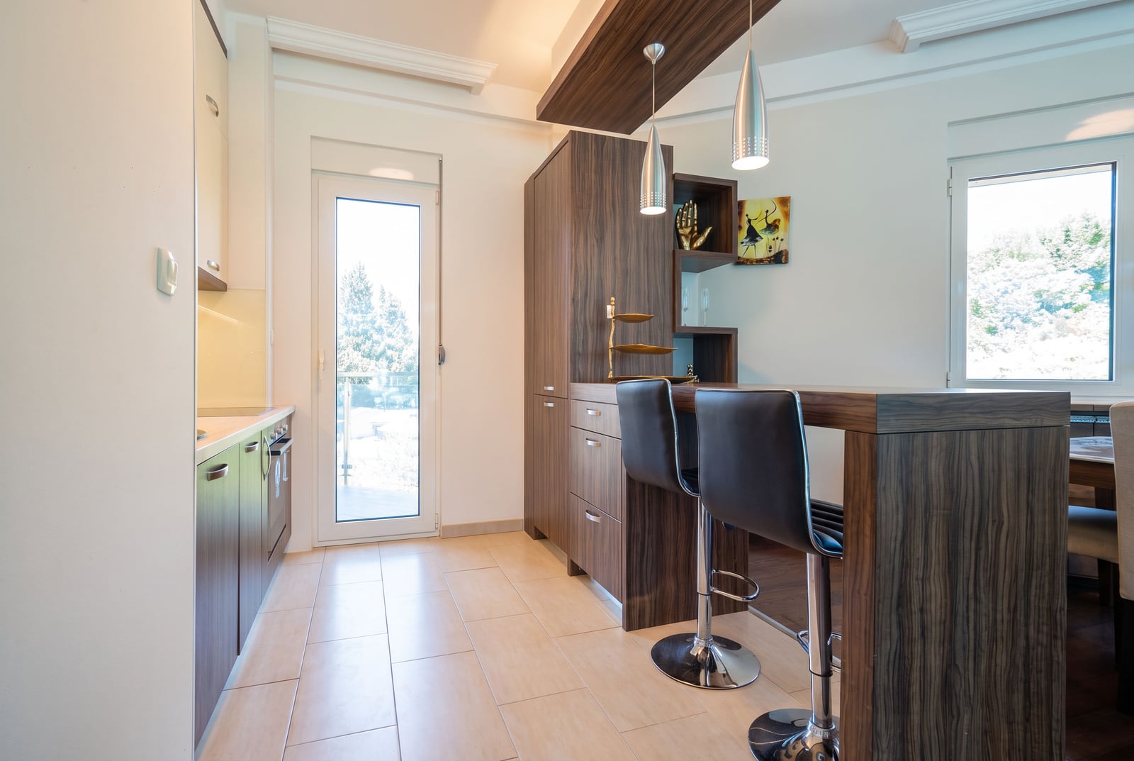 Modern kitchen featuring a dark wood breakfast bar, black leather stools, and pendant lights.