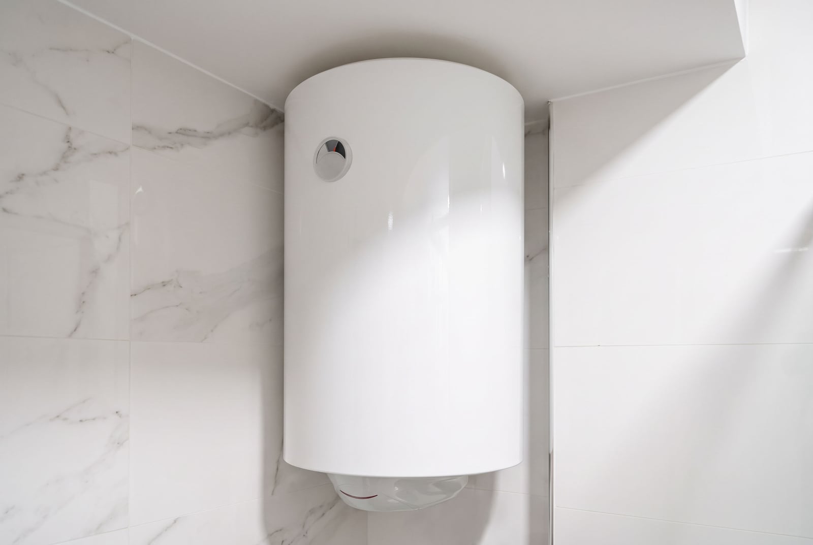 White cylindrical water heater mounted on a wall with marble-pattern tiles.