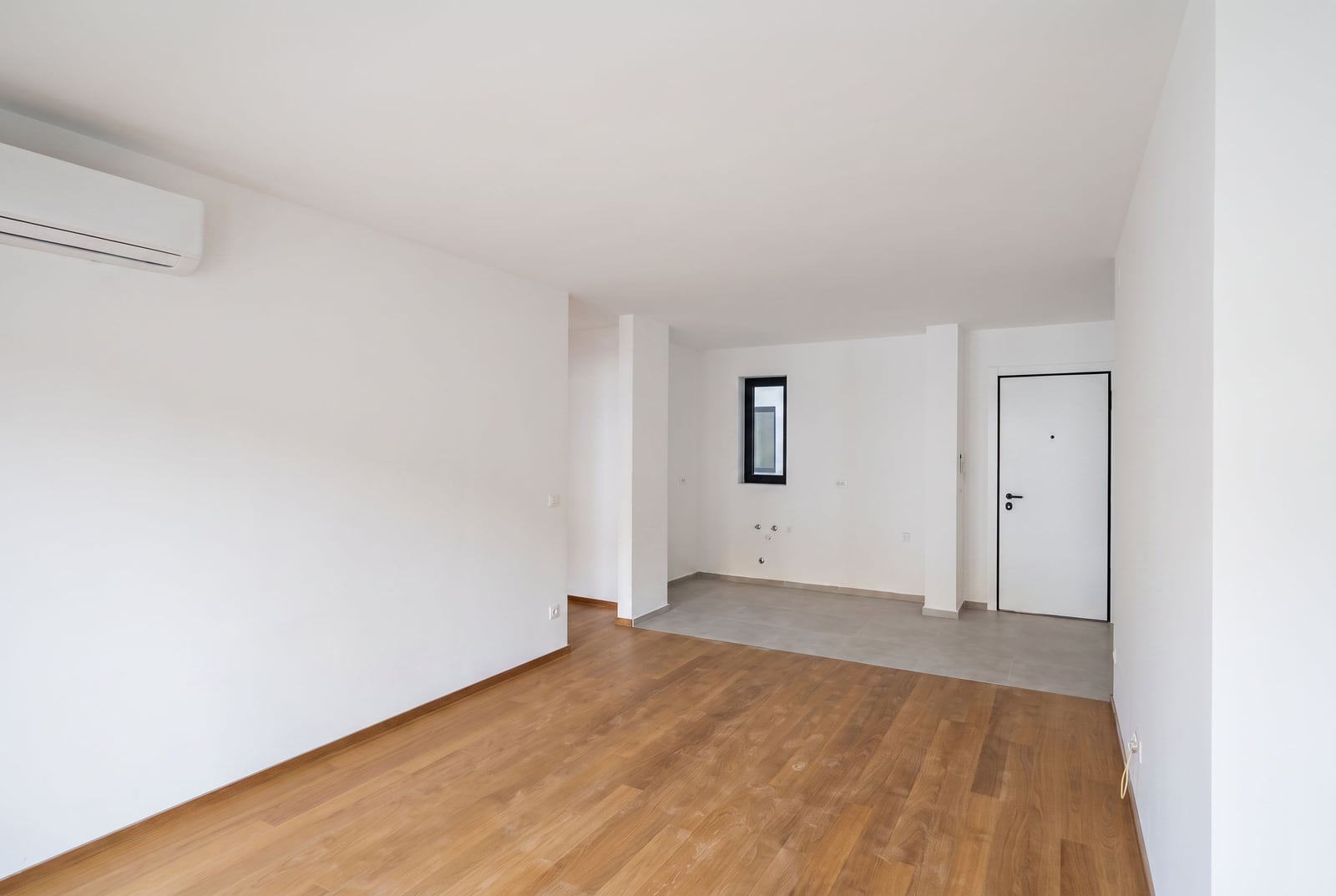 Bright living room with white walls, air conditioning, parquet flooring, and a kitchen area in an apartment in Budva, Montenegro.