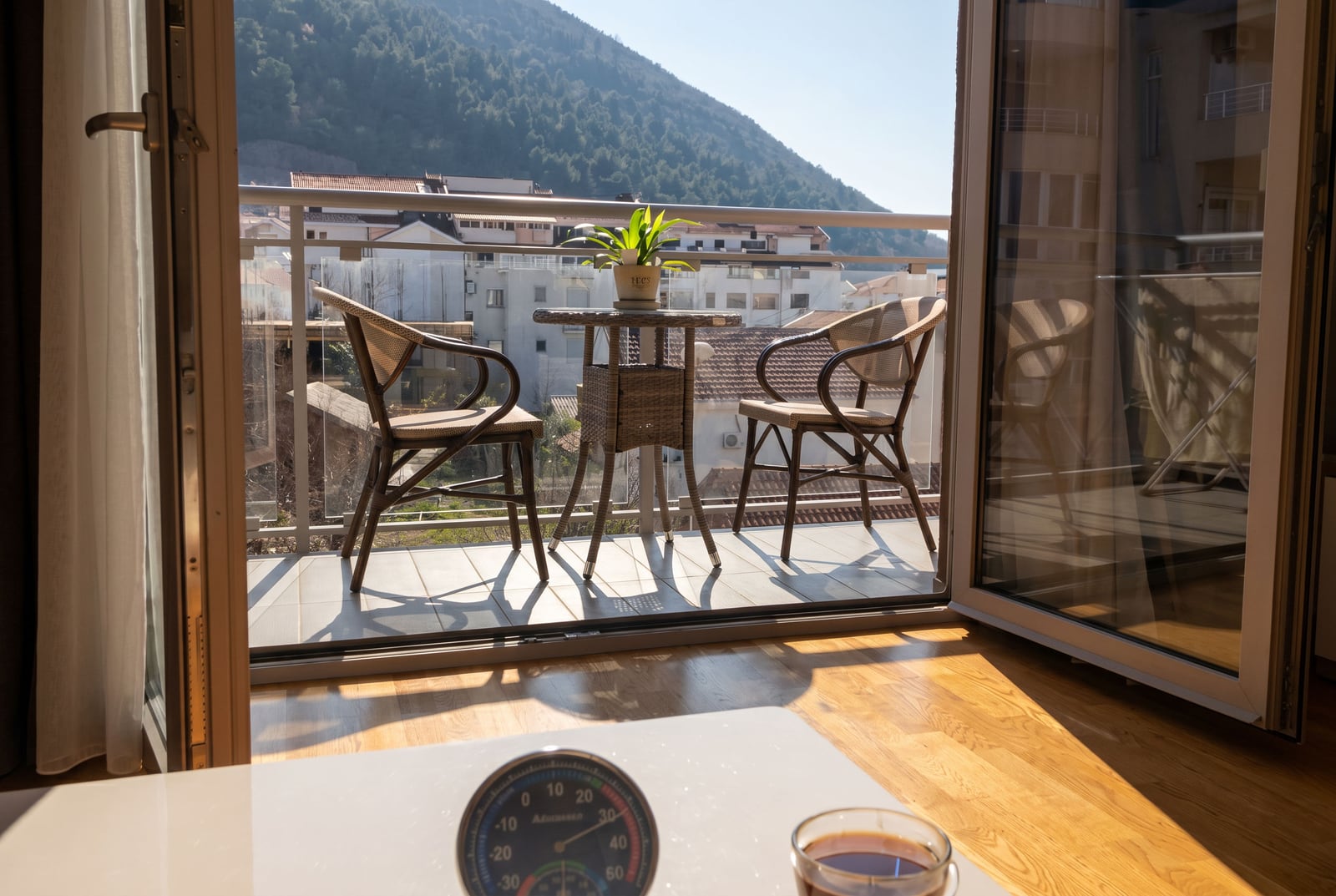 Balcony with wicker furniture and mountain views in an apartment in Budva, Montenegro: cozy terrace with panoramic glazing.