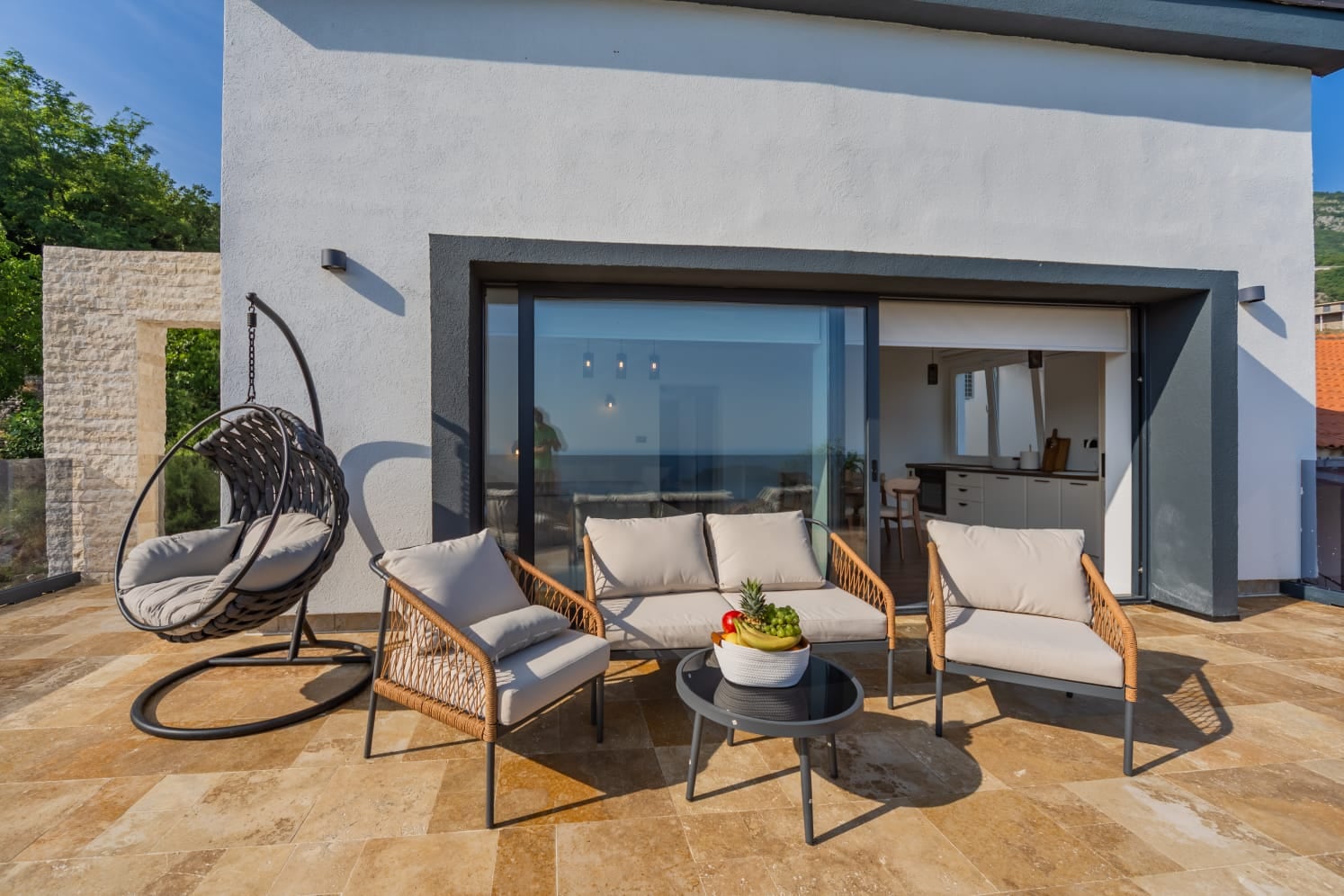 Villa terrace in Budva, Montenegro: wicker furniture, cocoon chair, and panoramic access to a modern living room.