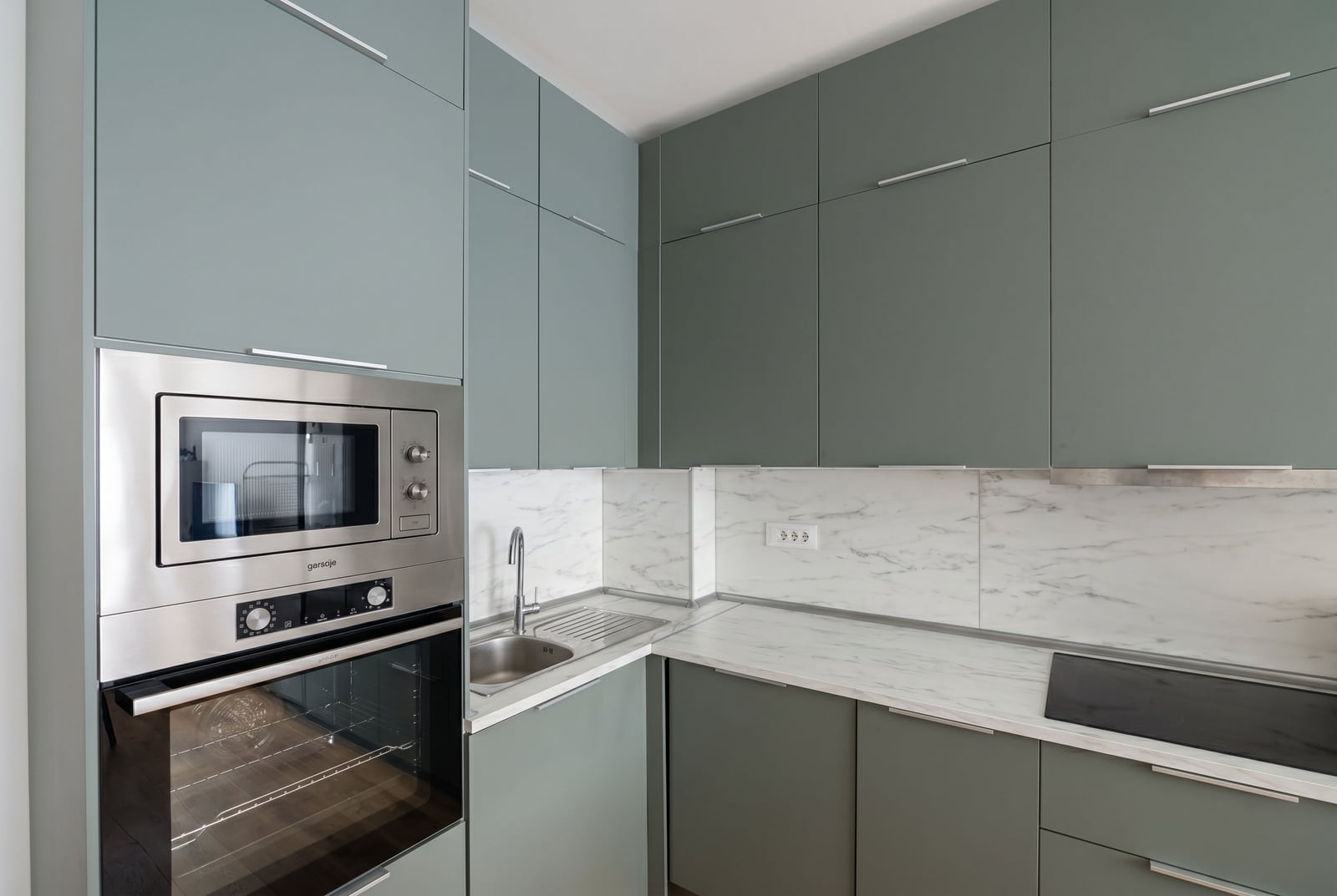 Modern kitchen in an apartment in Bečići, Montenegro: olive-colored cabinets, marble backsplash, and built-in Gorenje appliances.