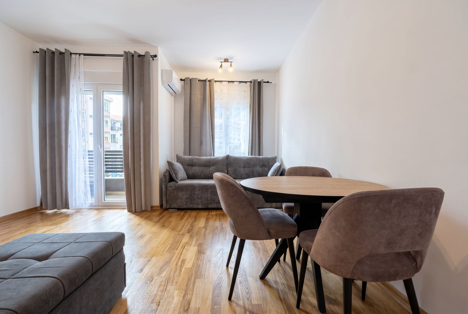 Bright living room with a round dining table, gray sofa, and parquet flooring in an apartment in Budva, Montenegro.