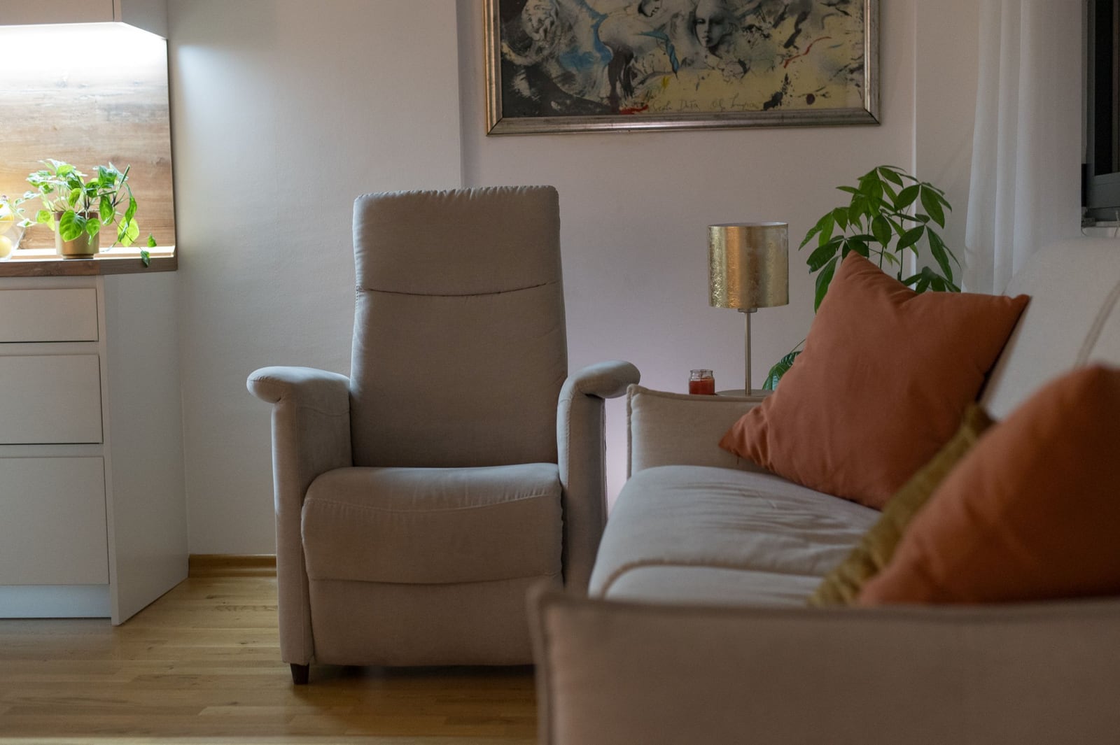 Cozy living room in a Tivat apartment, Montenegro: light-colored armchair, sofa with cushions, decor, and houseplants.