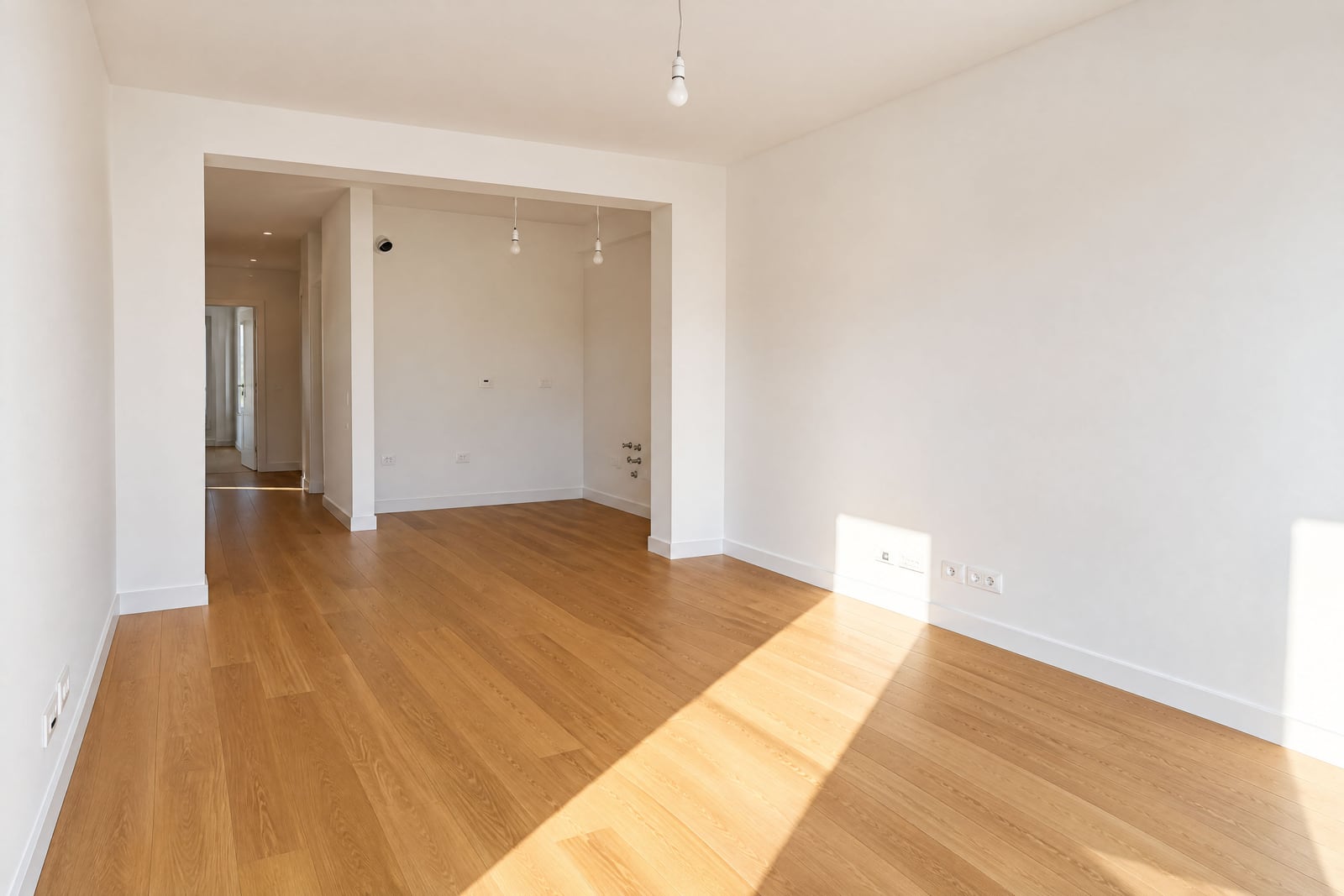 Empty room with wooden flooring and white walls, an archway leads to a hallway.