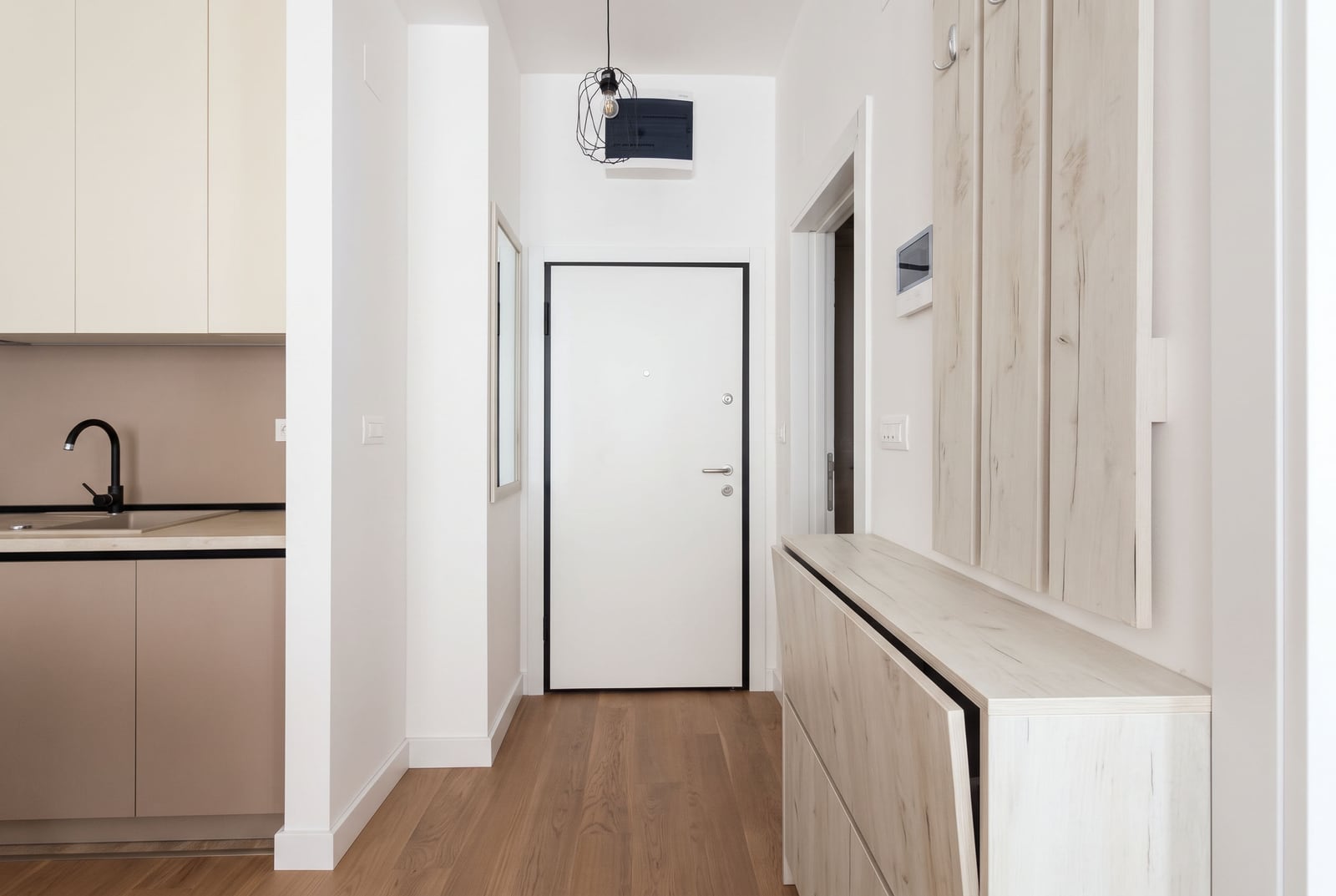 Hallway with an entrance door, light wood storage unit, and a partial view of a kitchen sink on the left.