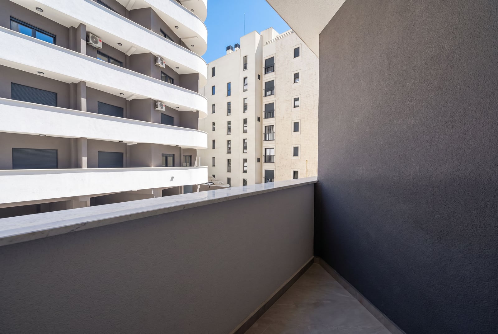 Empty balcony with a gray wall and marble ledge, overlooking adjacent multi-story residential buildings with curved balconies.