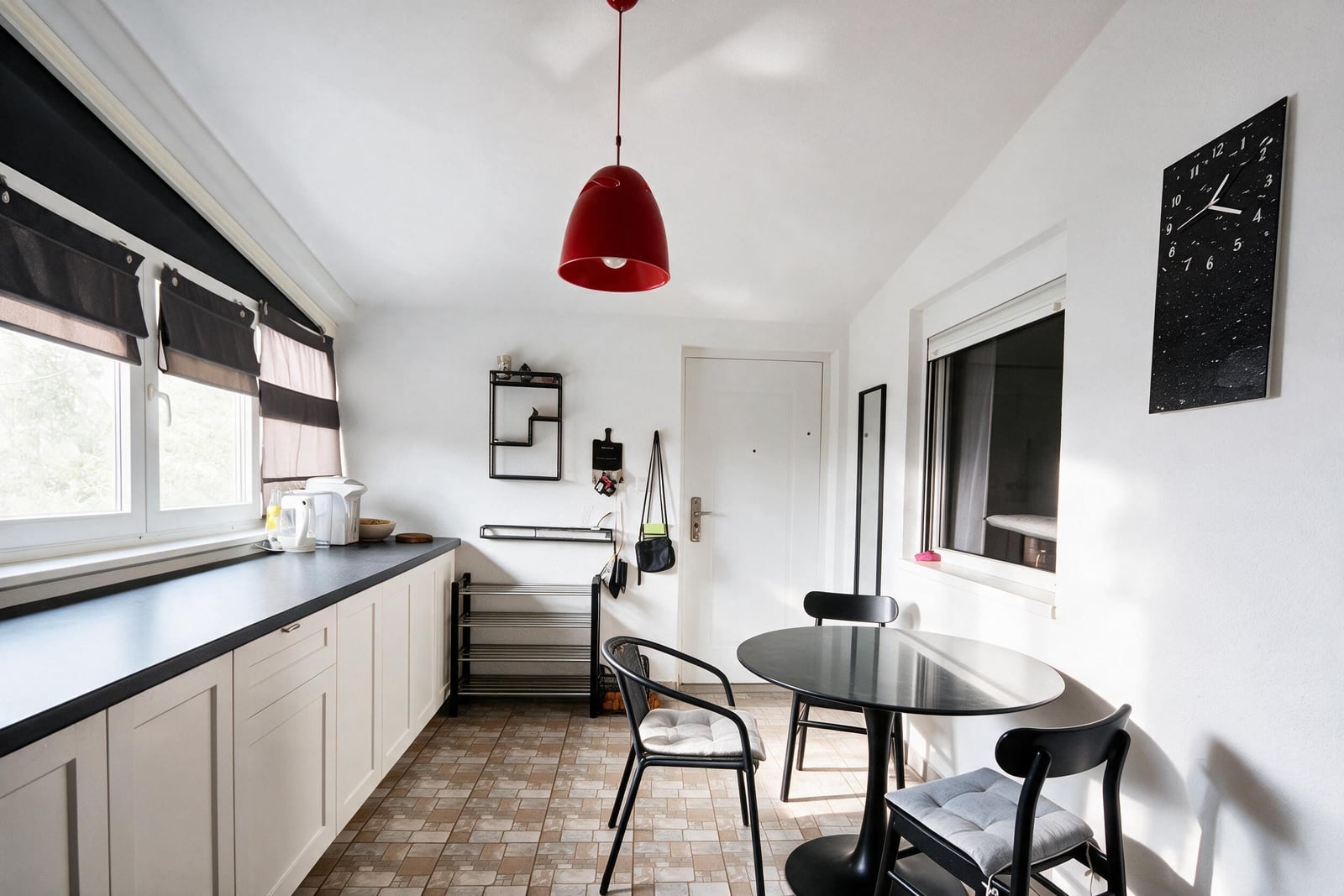 Kitchen with white cabinets, black countertop, red pendant light, and a round black dining table with chairs.