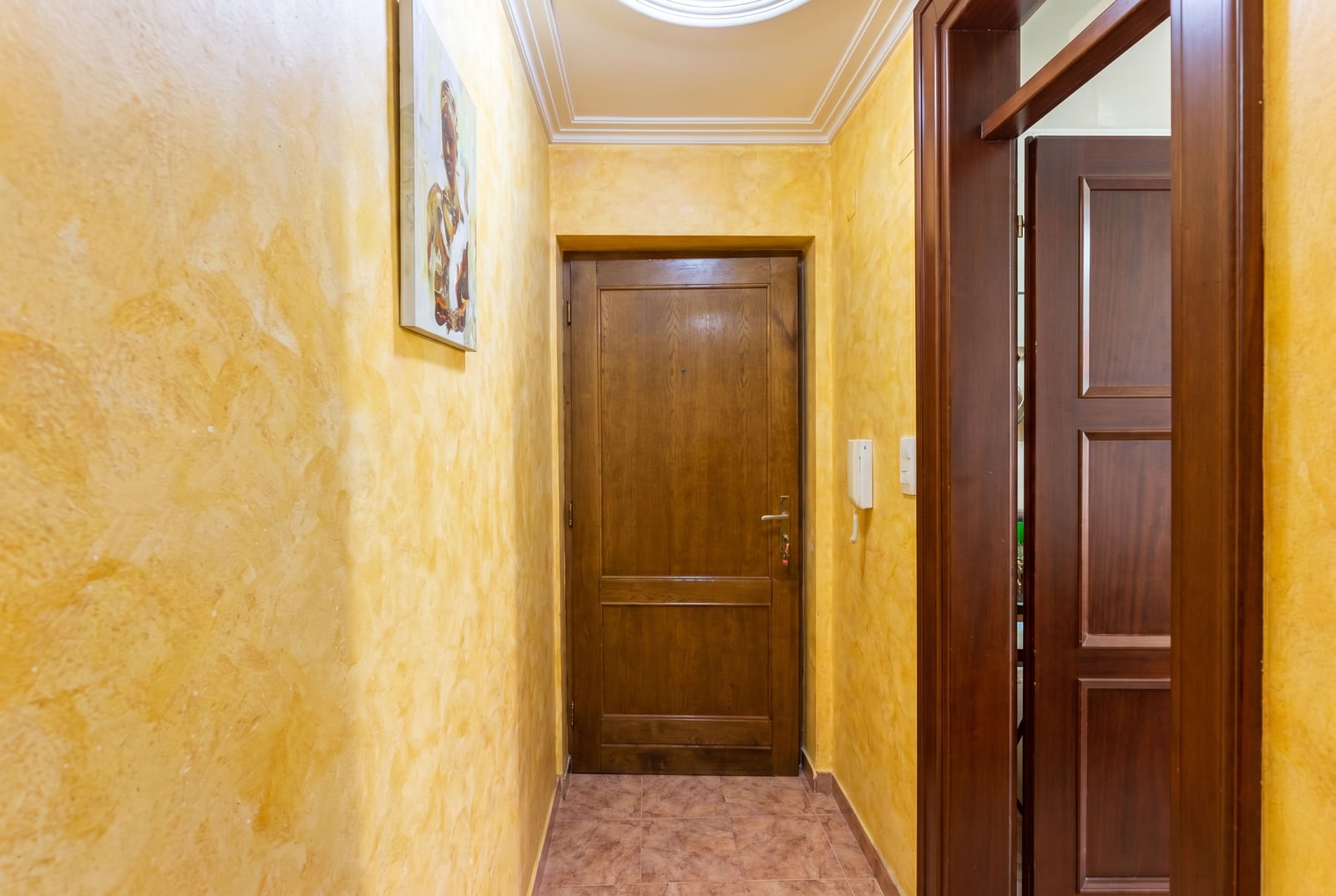 Entrance hall in a Budva apartment, Montenegro: yellow walls with decorative plaster, wooden doors, and tiled flooring.