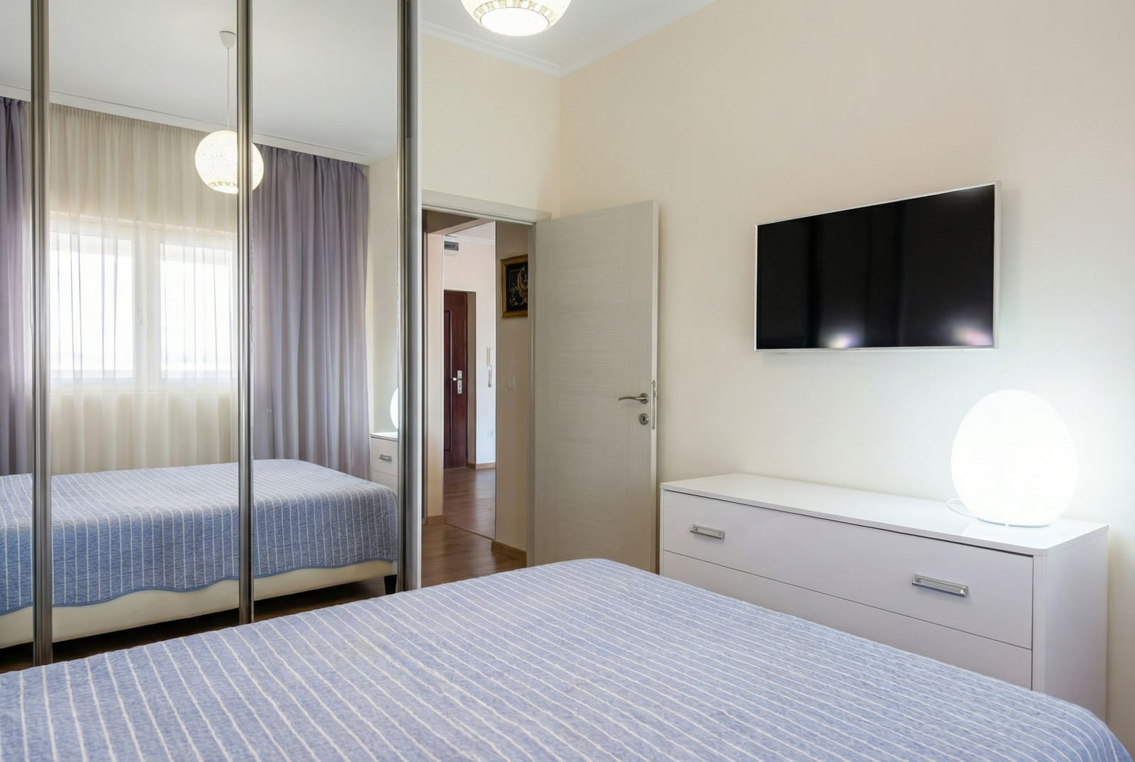 Bedroom in an apartment in Pržno, Montenegro: bed, mirrored sliding wardrobe, dresser, and wall-mounted TV in light tones.