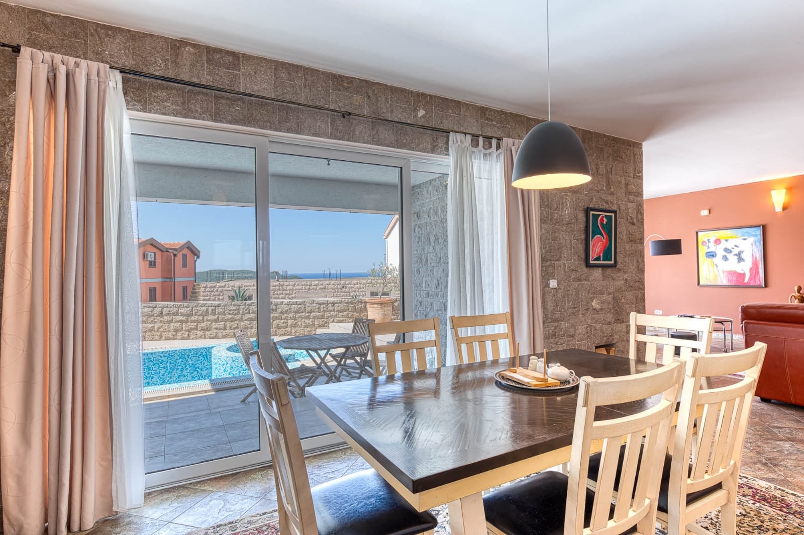 Living room with dining area in a villa in Bečići, Montenegro: view of the terrace with a pool and the sea through panoramic windows.