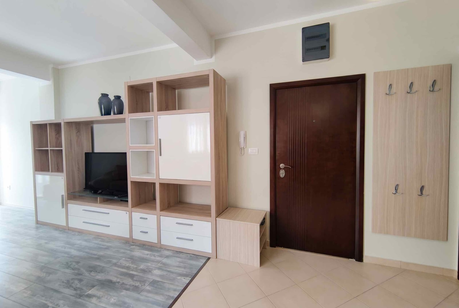 Living room in an apartment in Bečići, Montenegro: light-colored furniture, TV area, dark entrance door, and wall-mounted coat rack.