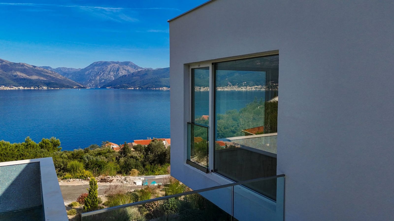 Modern villa in Krašići, Montenegro with panoramic views of the sea, mountains, and a glass balcony overlooking the bay.