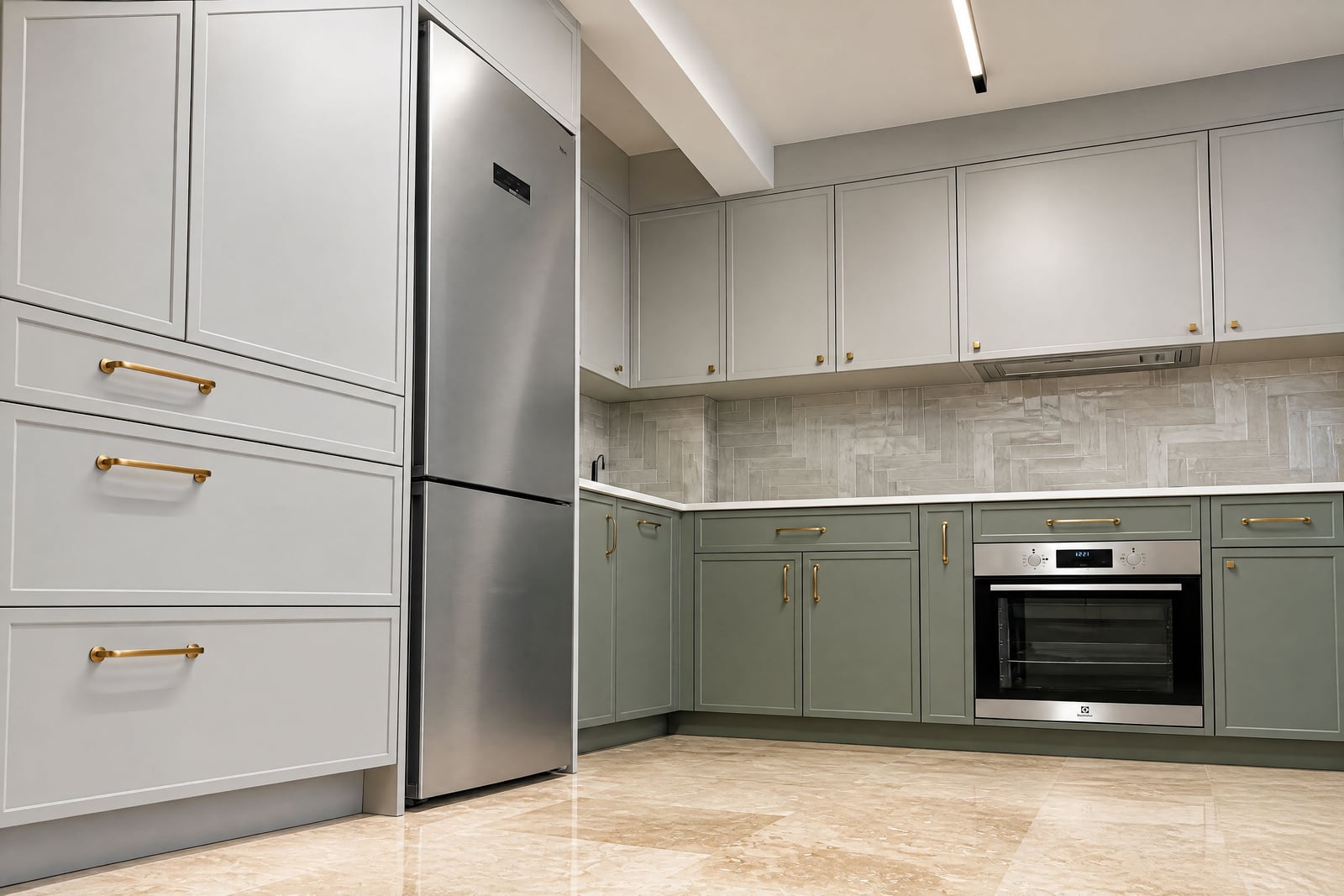 Modern kitchen with sage green cabinets, gold handles, built-in oven, stainless steel refrigerator, and herringbone tile backsplash.