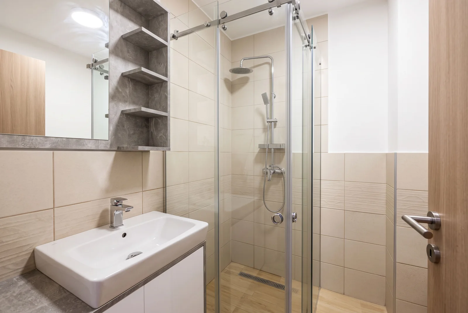 Modern bathroom featuring a glass shower enclosure, white vessel sink on a cabinet, and shelved mirror.