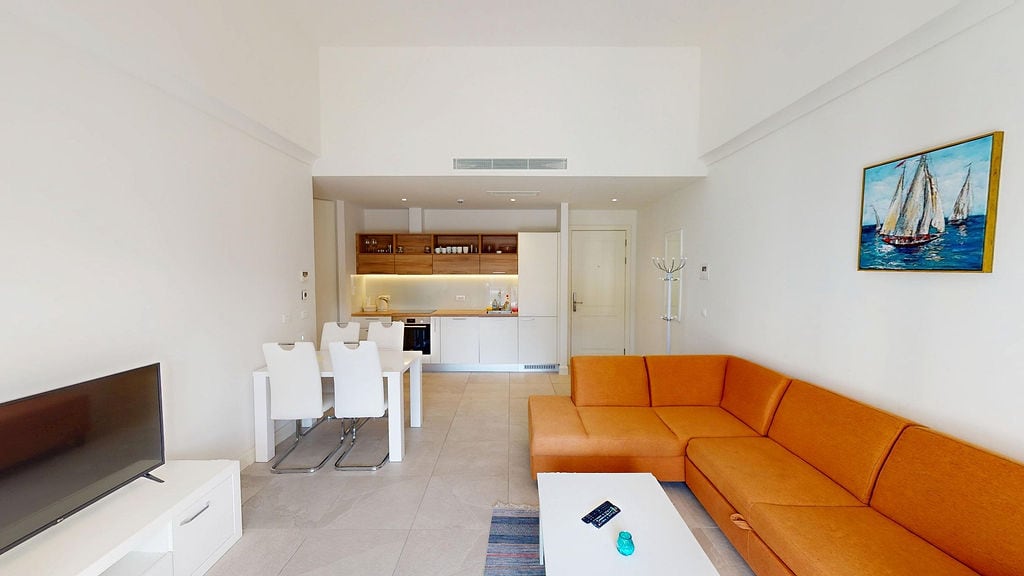 Modern living room with an orange sofa and kitchen in Lustica apartments, Montenegro: interior with dining area.