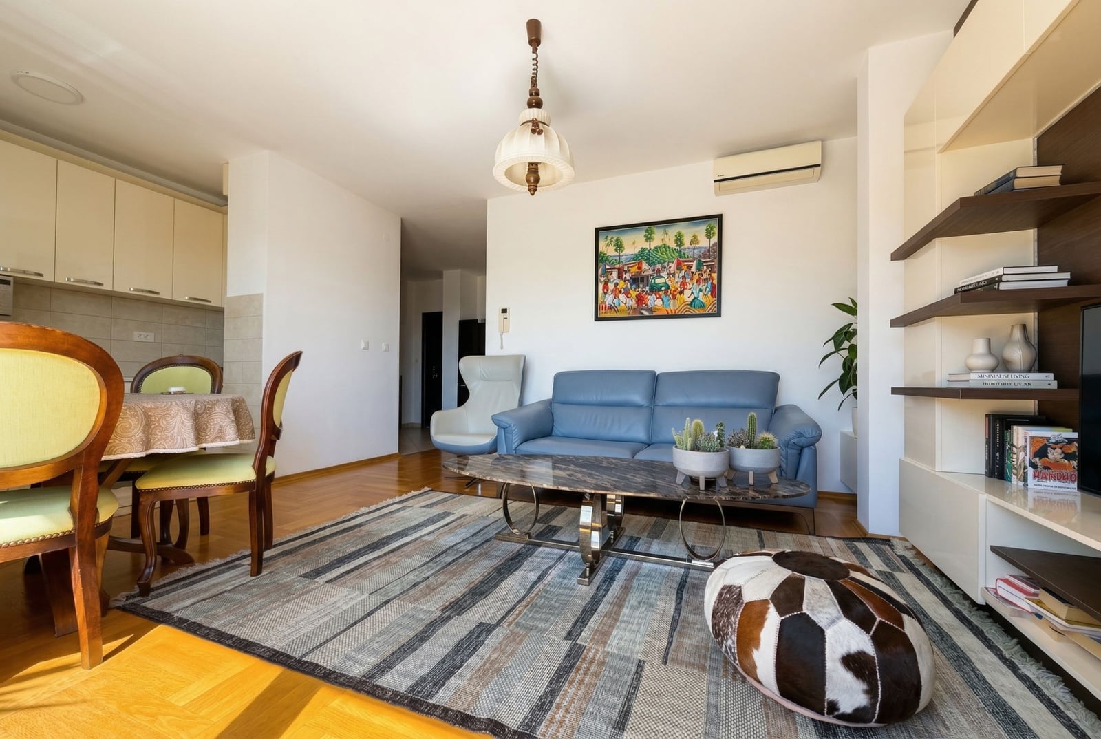 Living room with a blue leather sofa and dining area in an apartment in Budva, Montenegro: modern interior with parquet flooring.