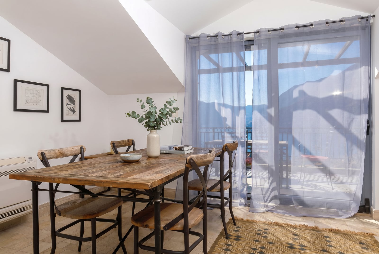 Dining area in a penthouse in Risan, Montenegro: wooden table, mountain and terrace views through panoramic windows.