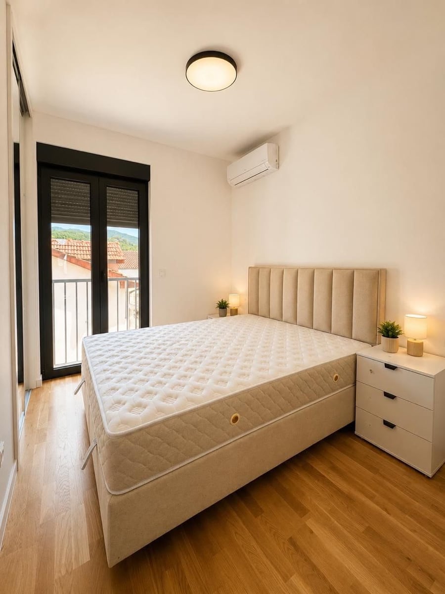 Modern bedroom with a double bed in a residential complex in Herceg Novi, Montenegro: bright interior, parquet flooring, and mountain view.