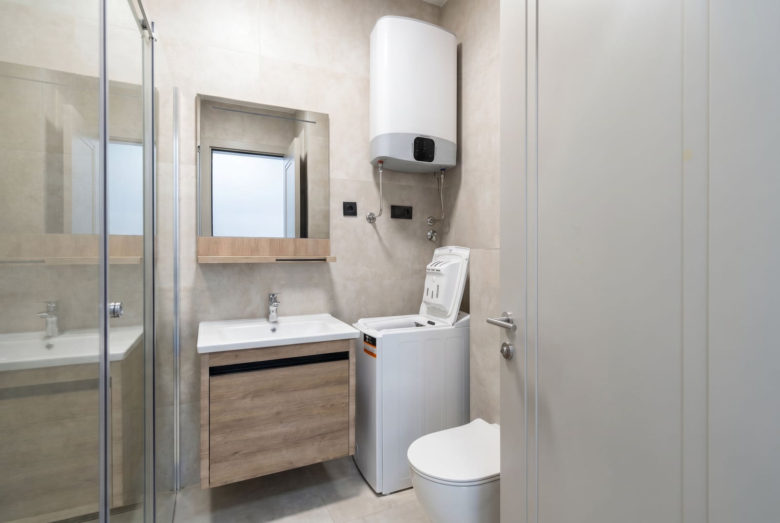 Modern bathroom in an apartment in Becici, Montenegro: walk-in shower, vanity unit with sink, and washing machine.