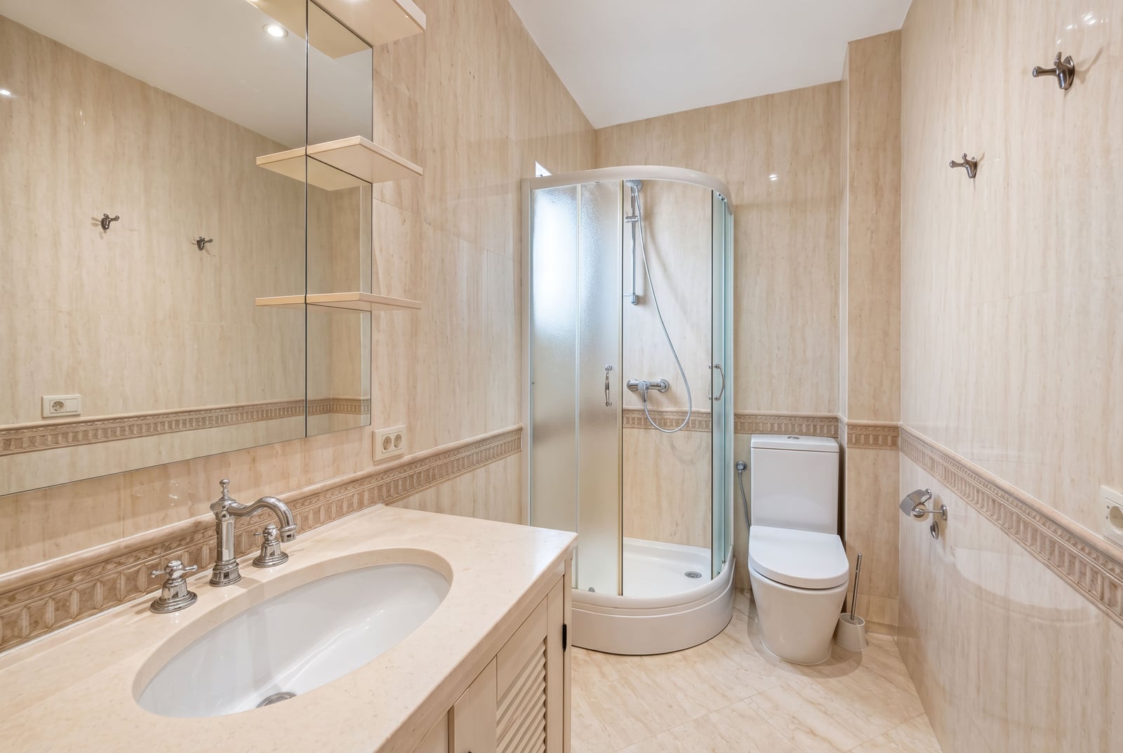 Bright bathroom with marble tiles, a sink vanity, corner shower enclosure, and toilet.