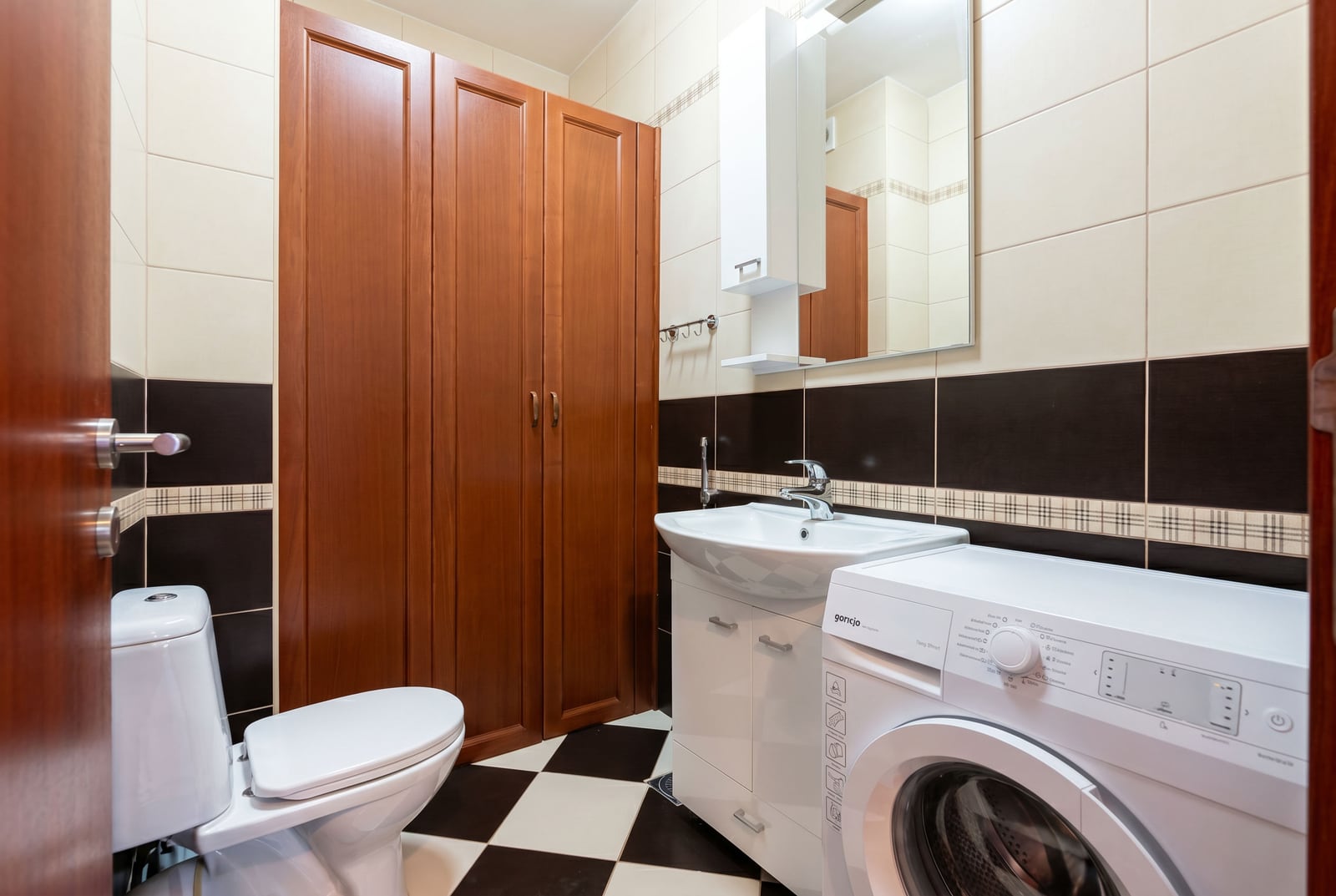 Bathroom in an apartment in Bar, Montenegro: checkerboard tile flooring, built-in cabinet, and washing machine.