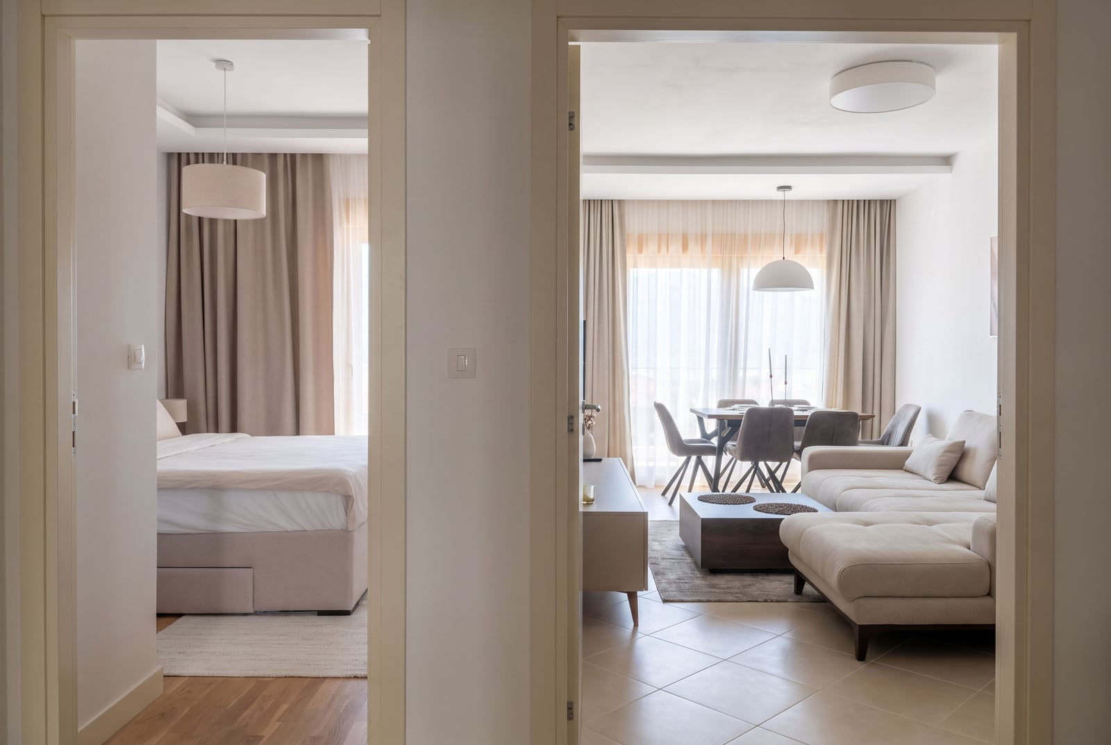 Modern apartment in Dobrota, Montenegro: view from the hallway into a bright living room with a sofa and a bedroom with a double bed.