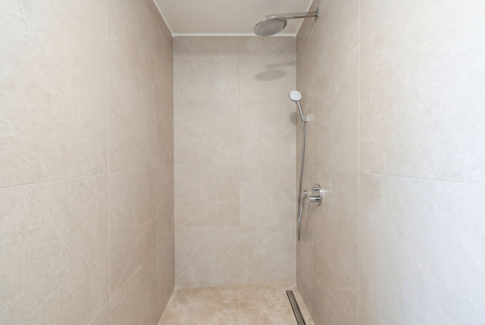 Modern shower cabin with beige tiles and a rainfall shower head in an office, Budva, Montenegro.